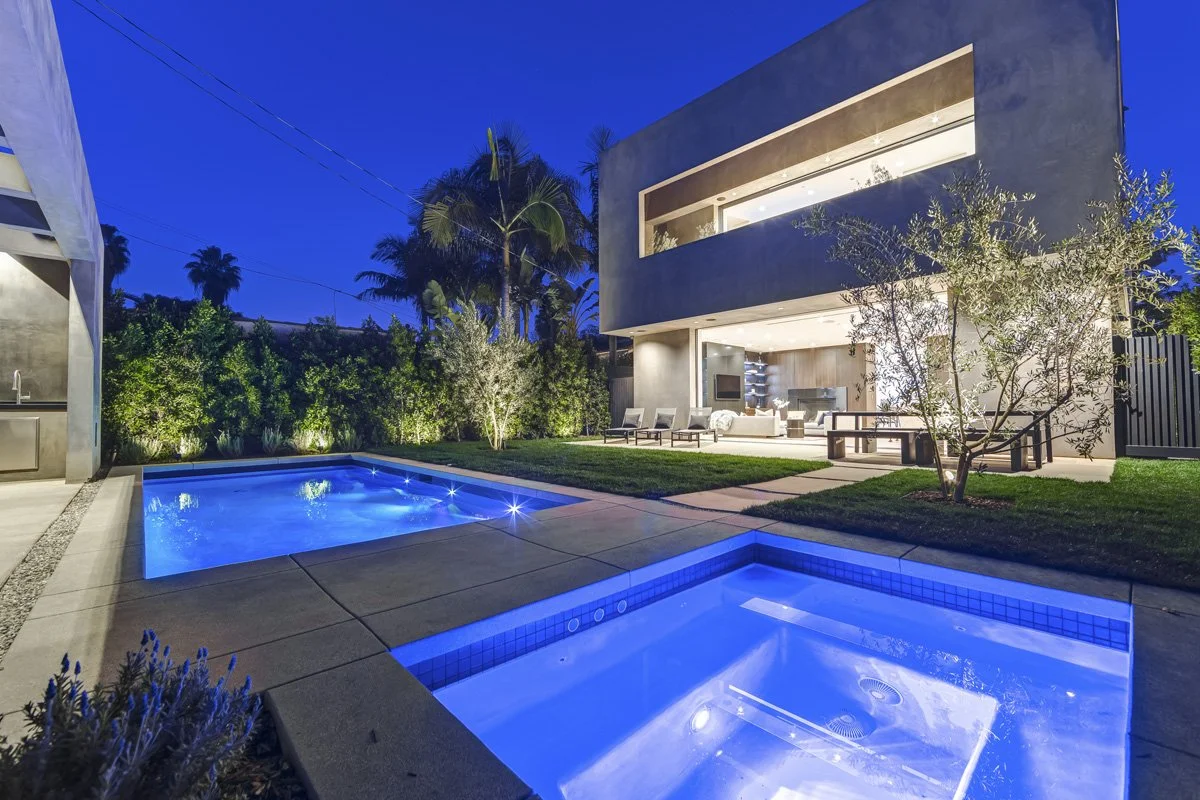 West Hollywood custom home backyard with modern pool and spa, open glass living room, and landscaped courtyard at night