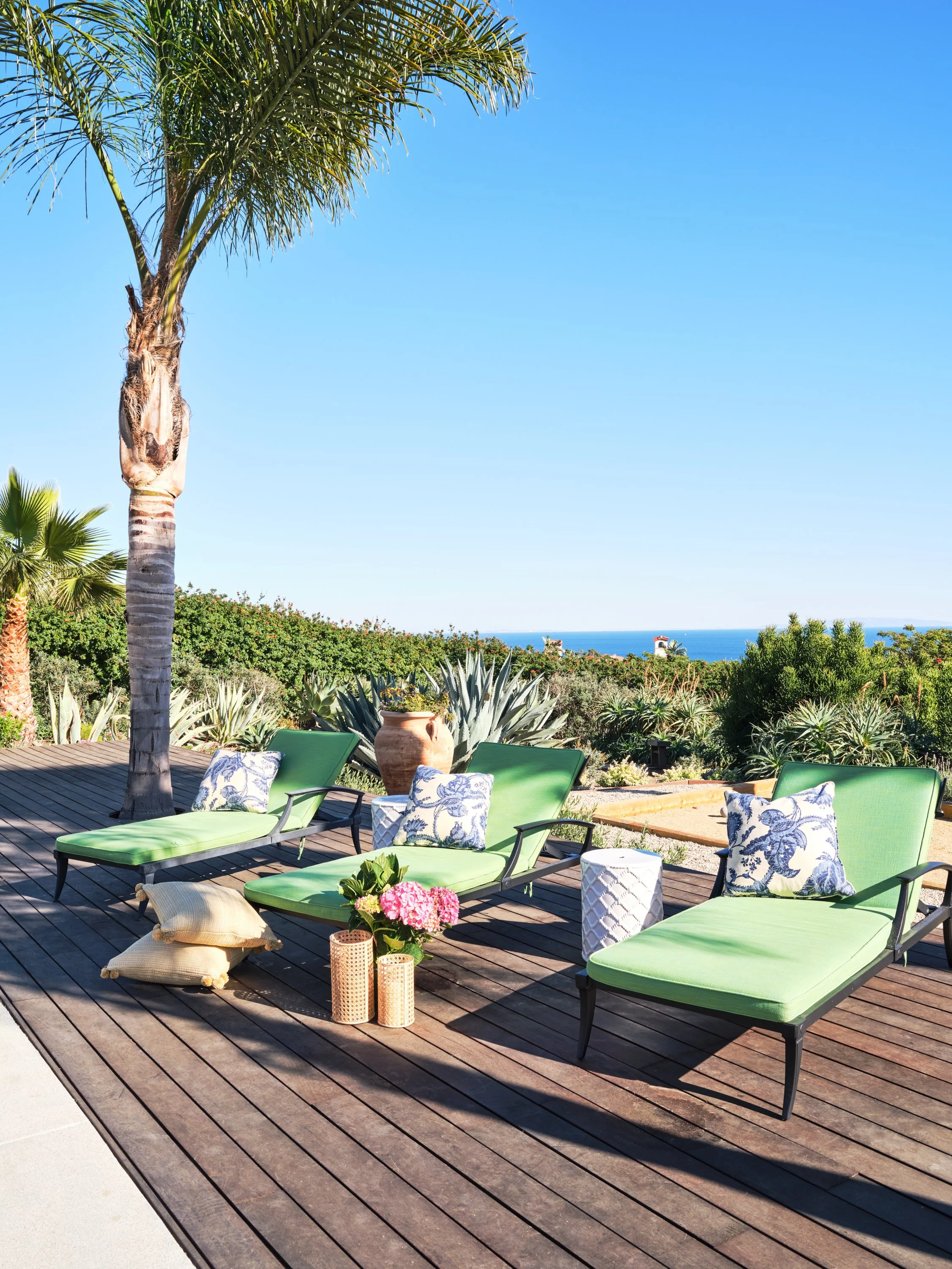 Malibu custom home outdoor deck with green chaise loungers, ocean views, palm trees, and coastal landscaping built by Heart Construction