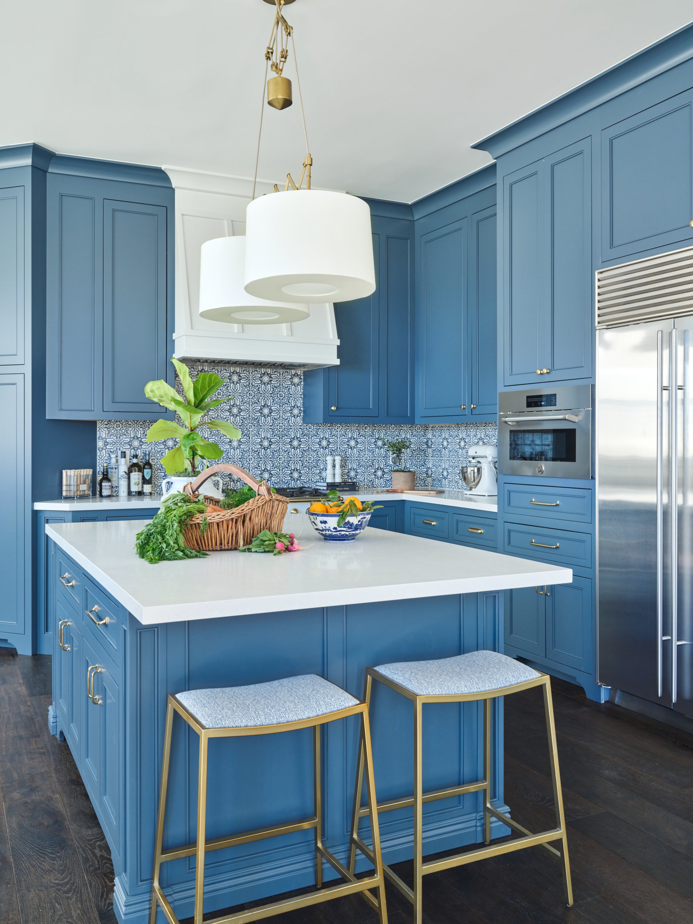 Malibu custom kitchen island with blue cabinetry, quartz countertop, brass hardware, upholstered bar stools, and statement pendant lighting by Heart Construction