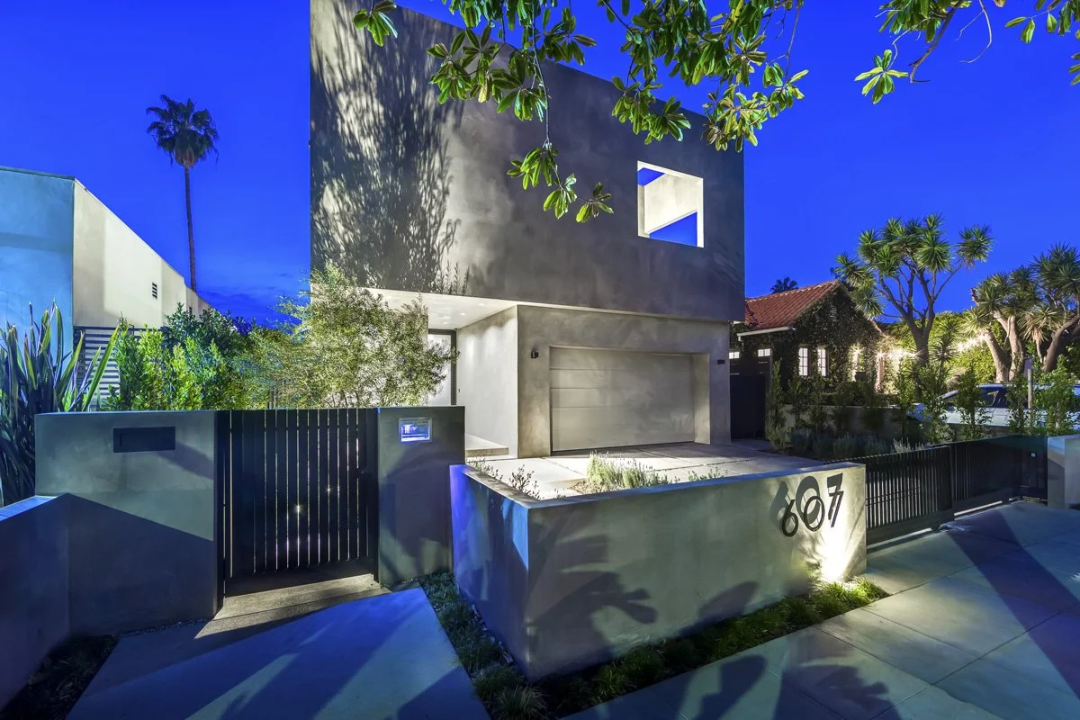 West Hollywood custom home exterior at night with concrete façade, illuminated entry, and modern gated front yard