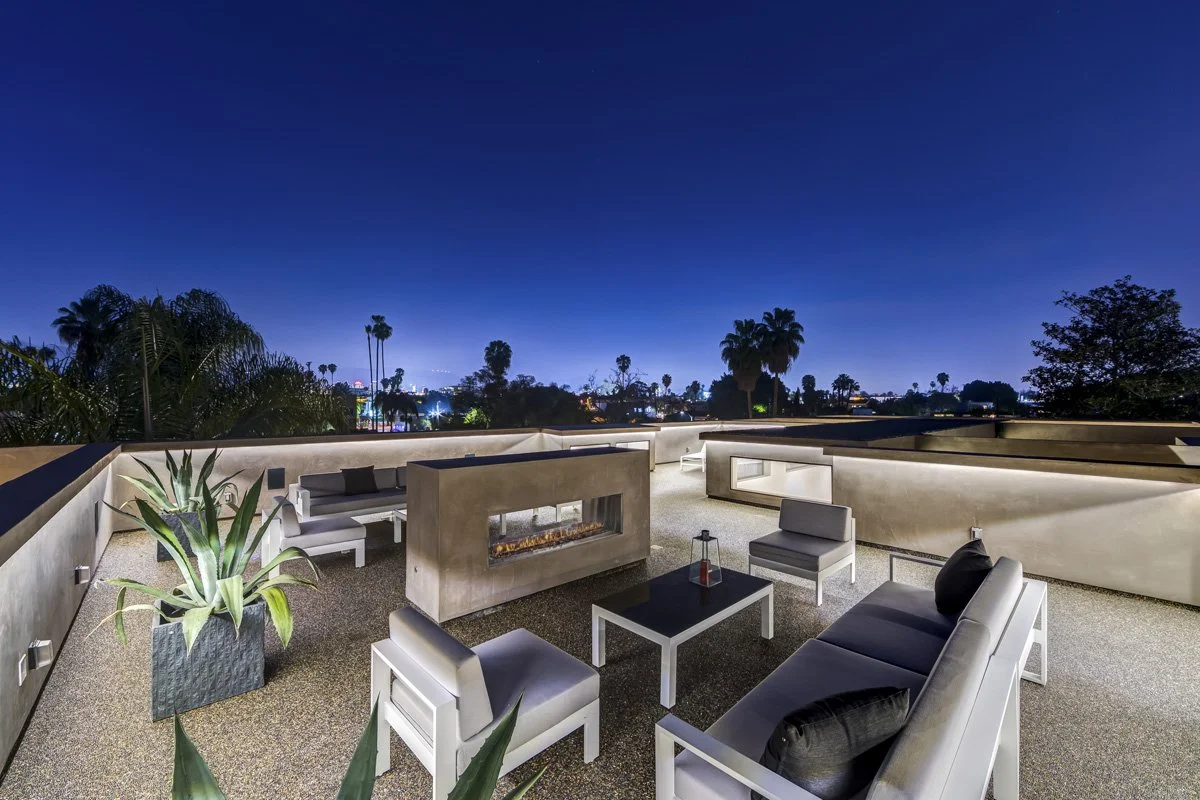 Modern rooftop terrace at night with built-in linear fire feature and panoramic Los Angeles city views