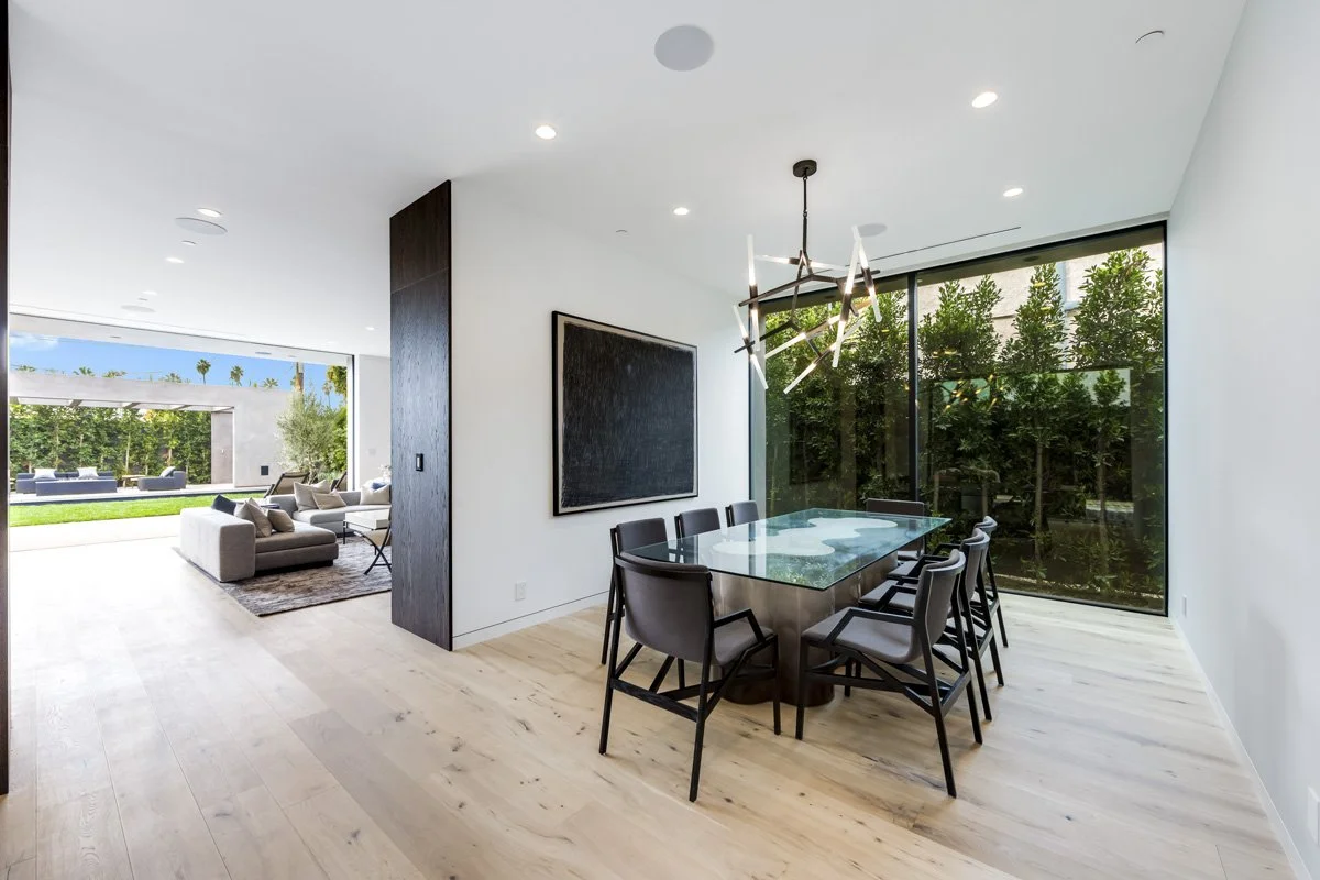 West Hollywood custom home dining room with glass table, floor-to-ceiling windows, and open connection to backyard pavilion