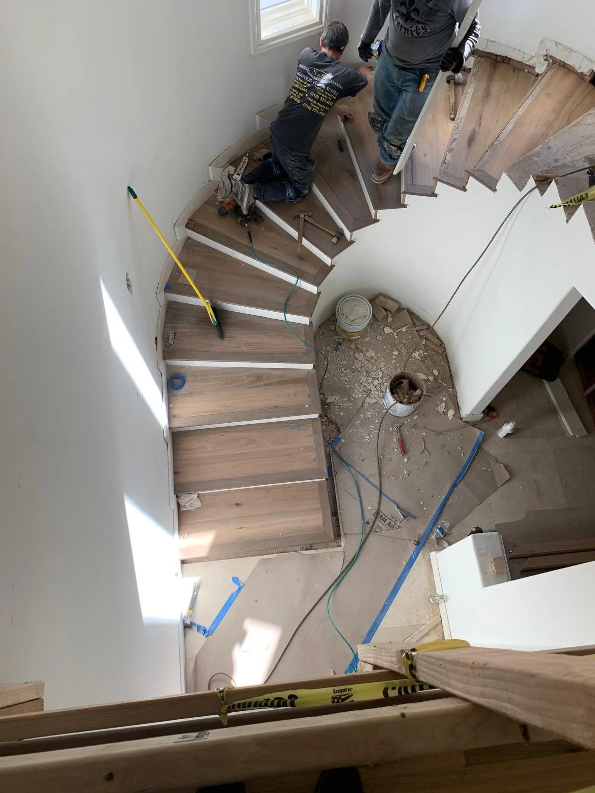Curved staircase installation in Brentwood custom home with wood treads and construction work in progress