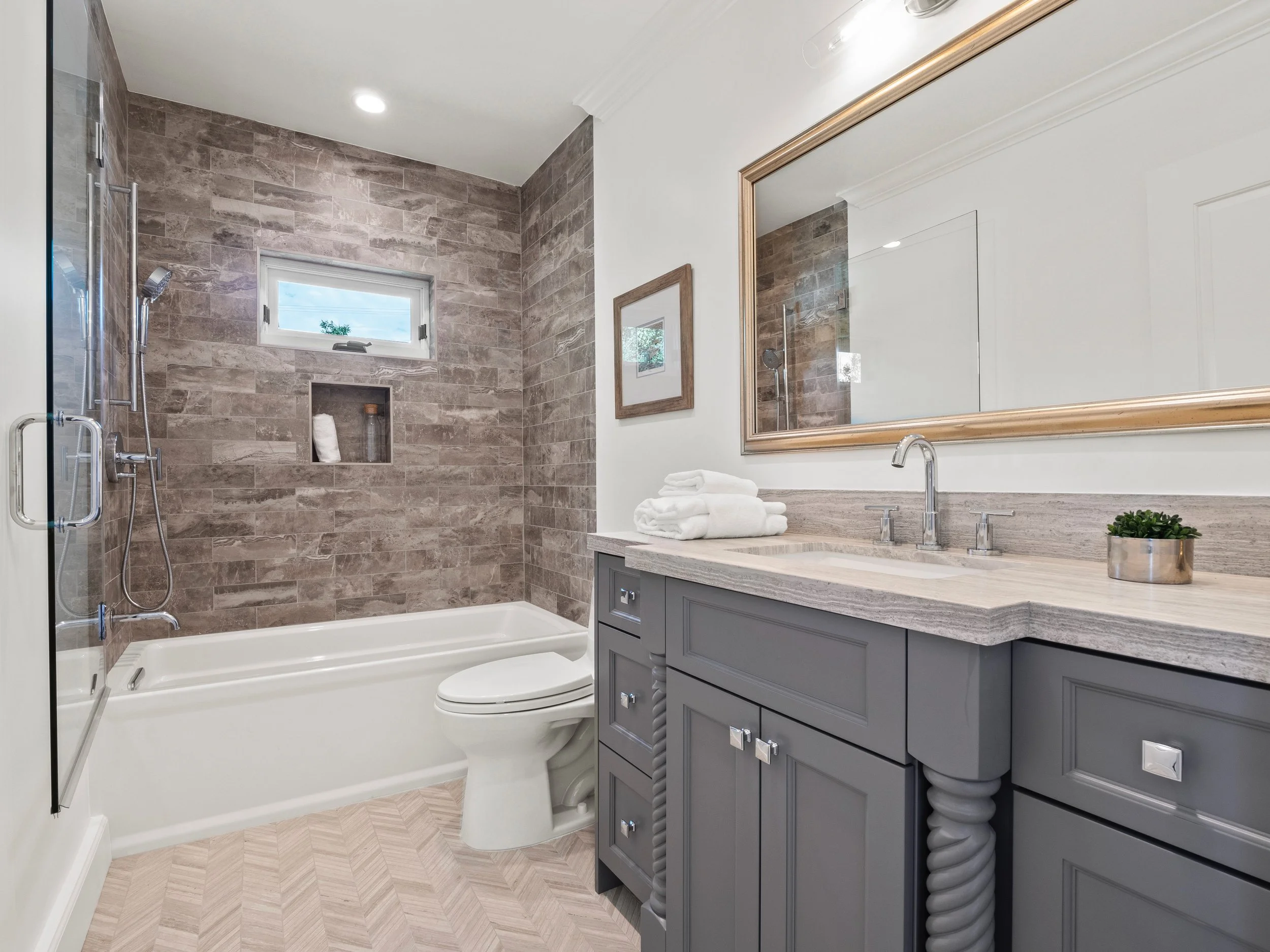 Hancock Park guest bathroom with gray shaker vanity, stone countertop, framed mirror, and tub-shower combo with textured tile surround and built-in niche.