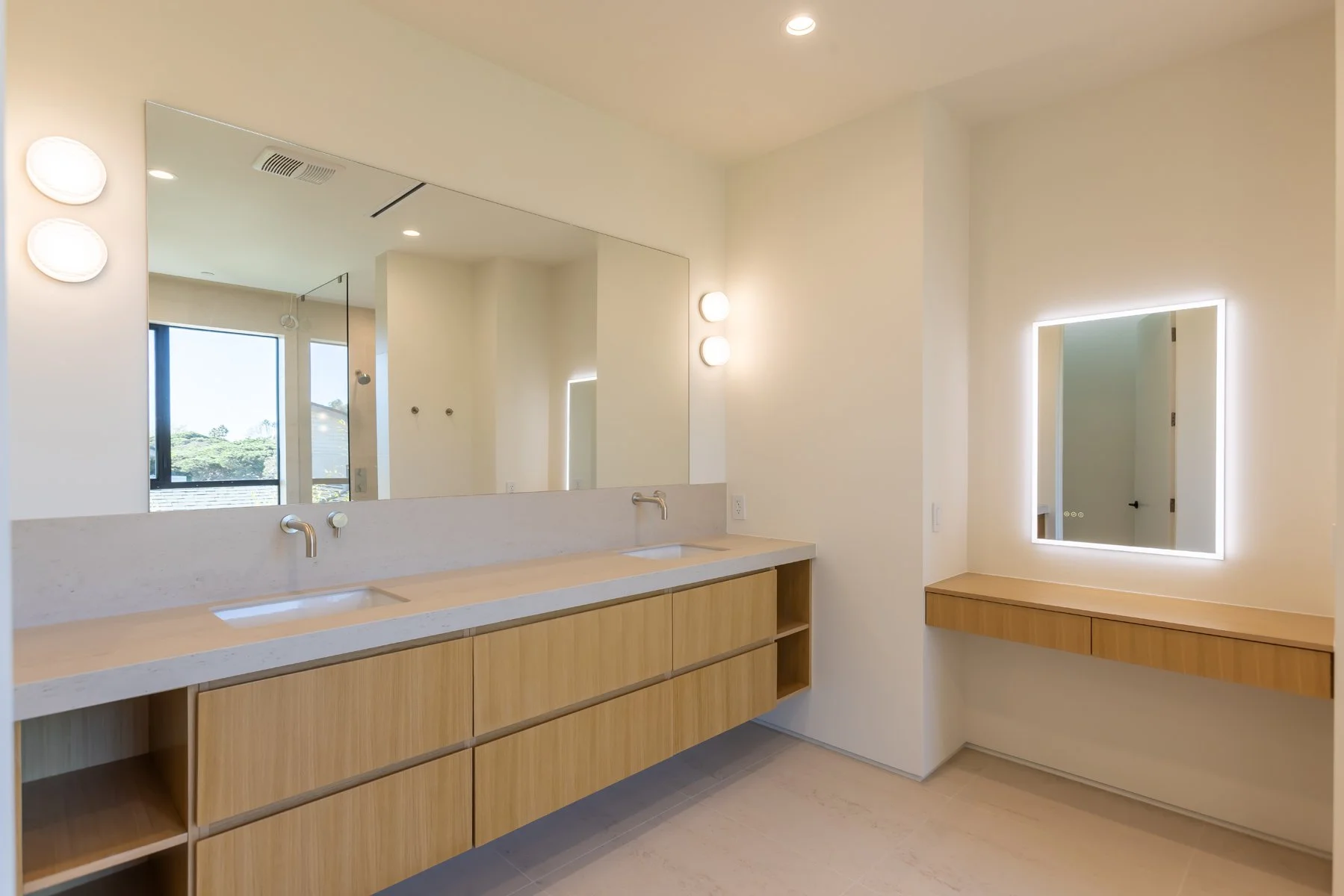 Modern double-sink bathroom vanity with custom light wood cabinetry, integrated stone countertops, and full-width mirror with soft sconces in a Mar Vista home remodel by Heart Construction.