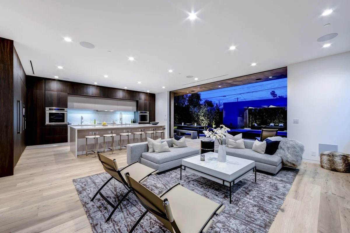 West Hollywood custom home open-concept living room and kitchen with sliding glass walls opening to illuminated backyard at night