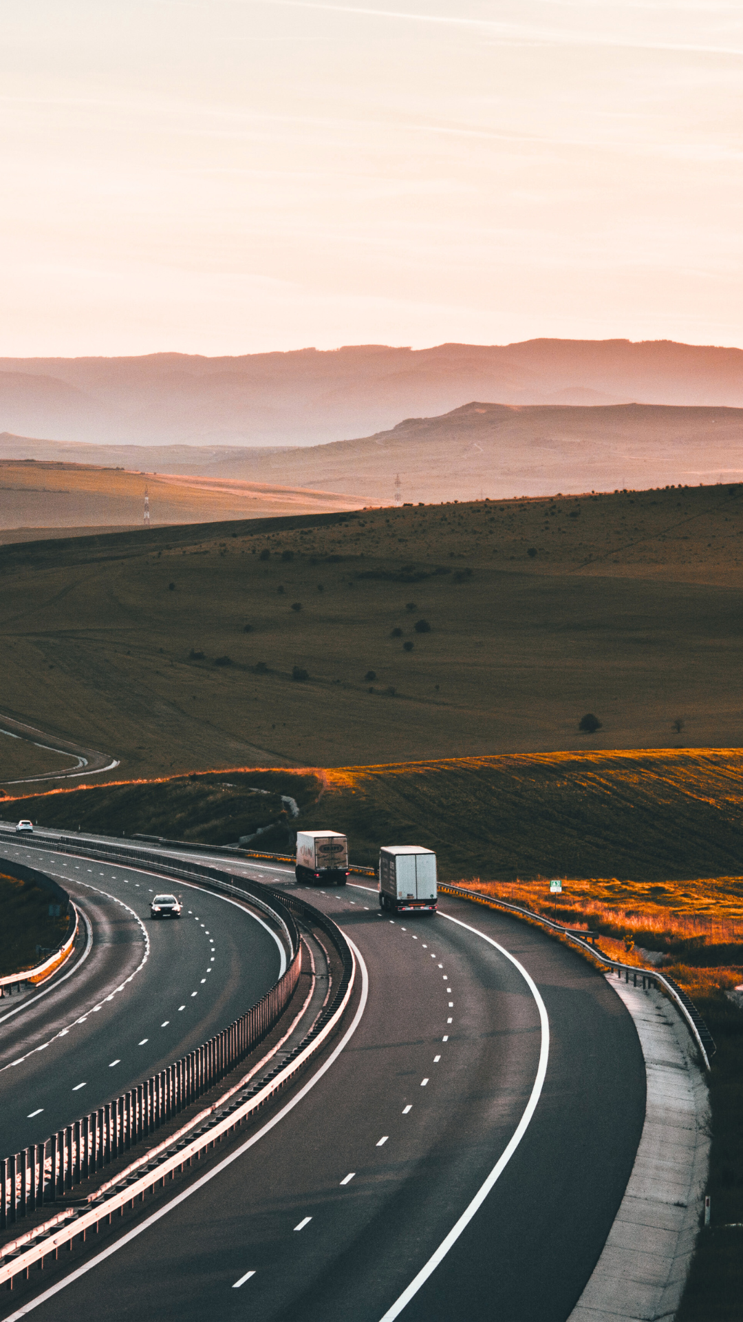 Carretera en una zona montañosa con vehículos en movimiento durante el atardecer.