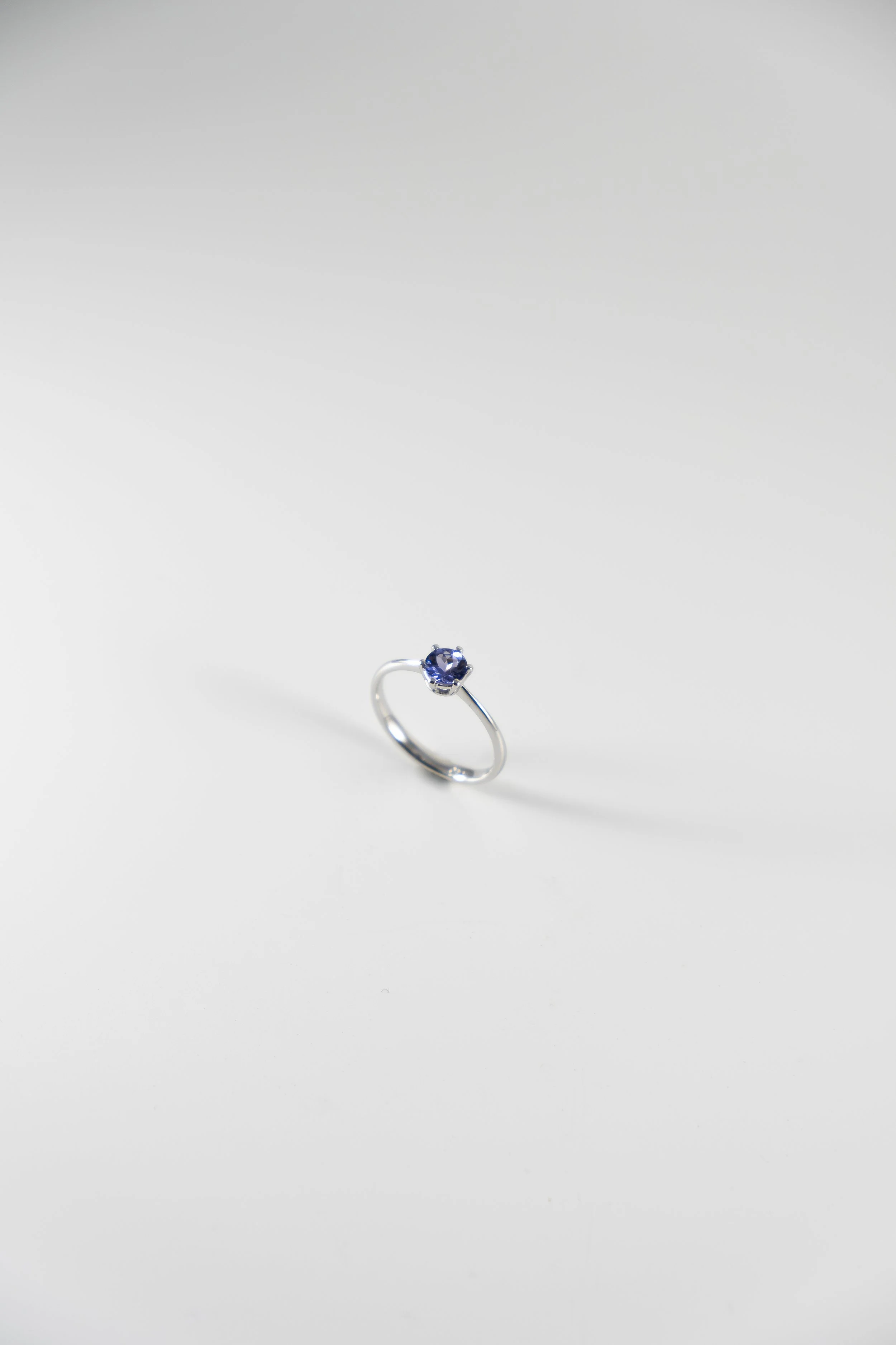 A silver ring with a round purple gemstone set in the center, displayed on a plain white background.
