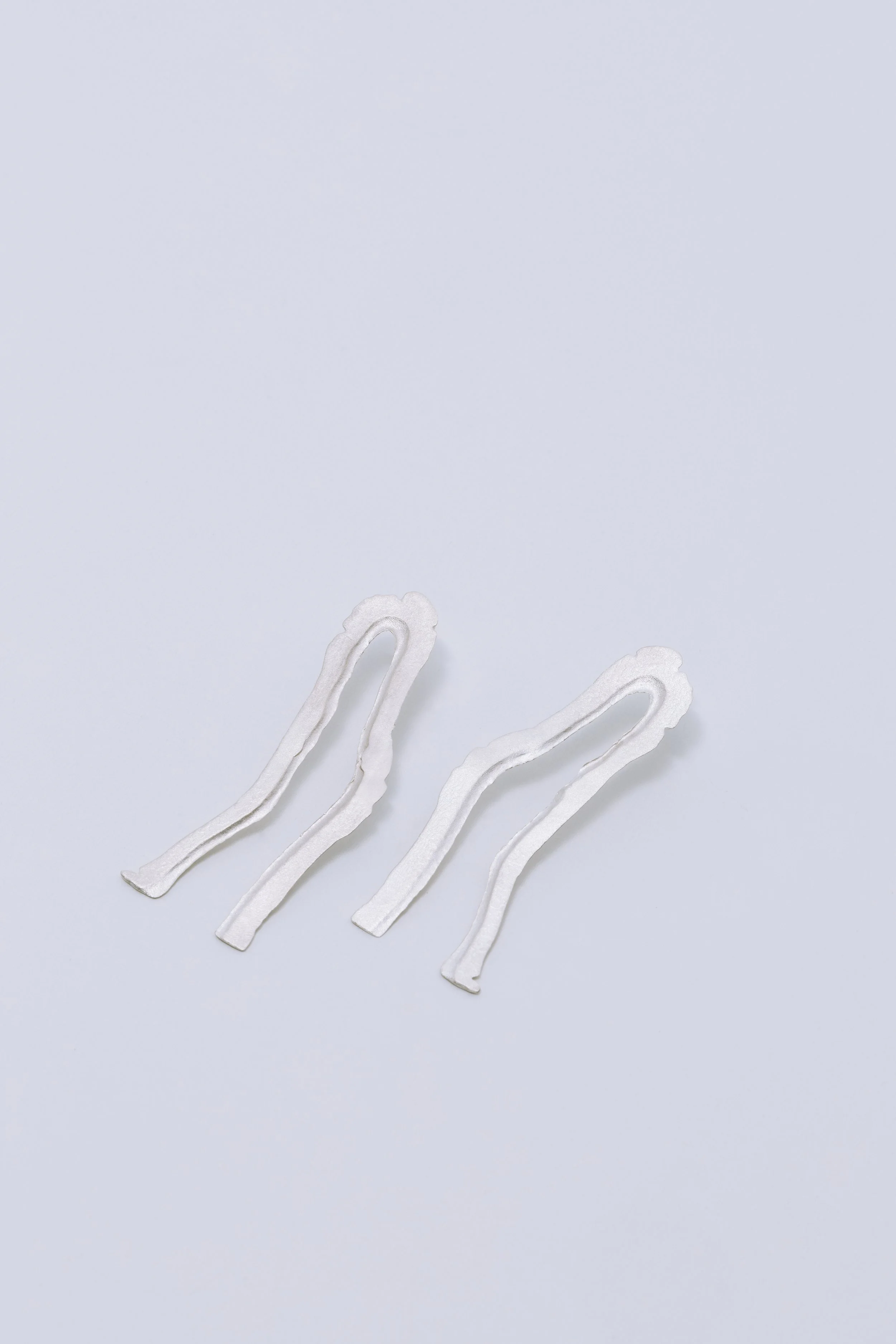 Pair of 925 sterling silver earrings from the Fleeting Fragments series, showing delicate, organic surface textures with fine, fluid lines.