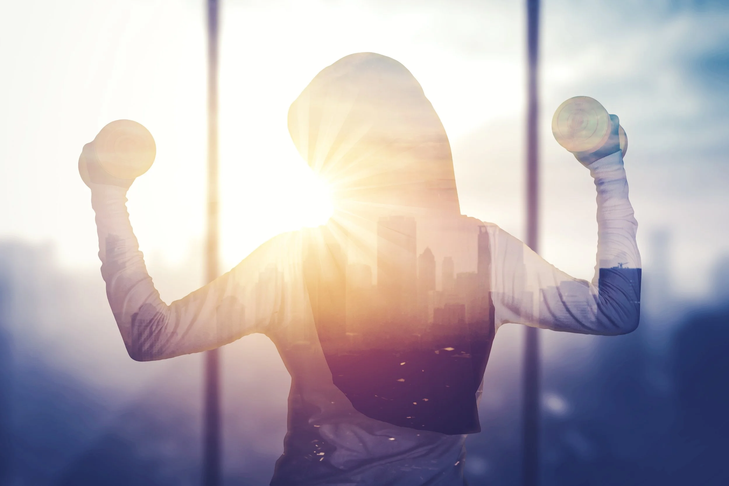 Silhouette of a woman lifting two small dumbbells with sunlight shining behind her, creating a bright, glowing effect and a city skyline reflection.