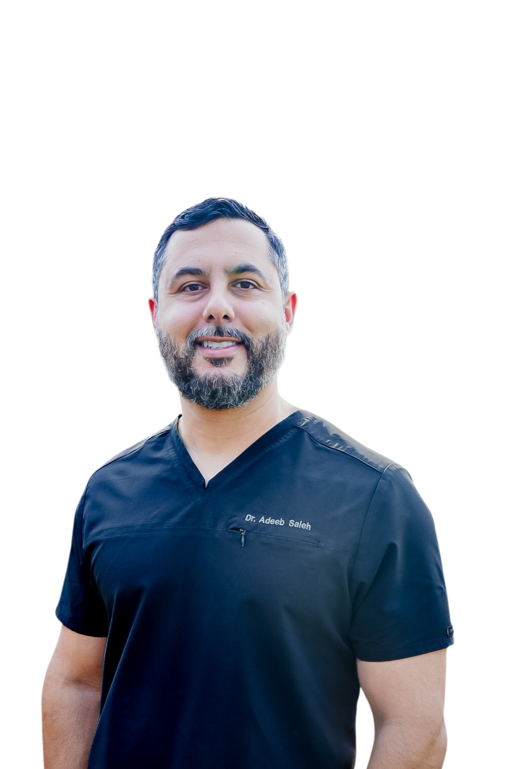 A smiling man with a beard wearing black medical scrubs that have the name 'Dr. Adeeb Saleh' embroidered on the chest, standing outdoors.