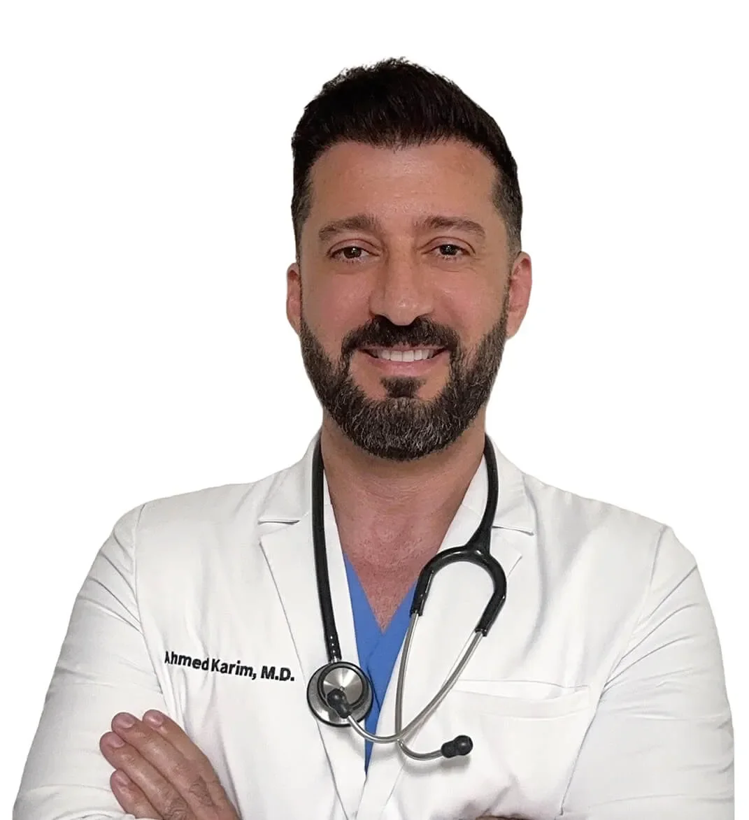 A male doctor with a beard and short dark hair, smiling with arms crossed, wearing a white coat with a stethoscope around his neck.