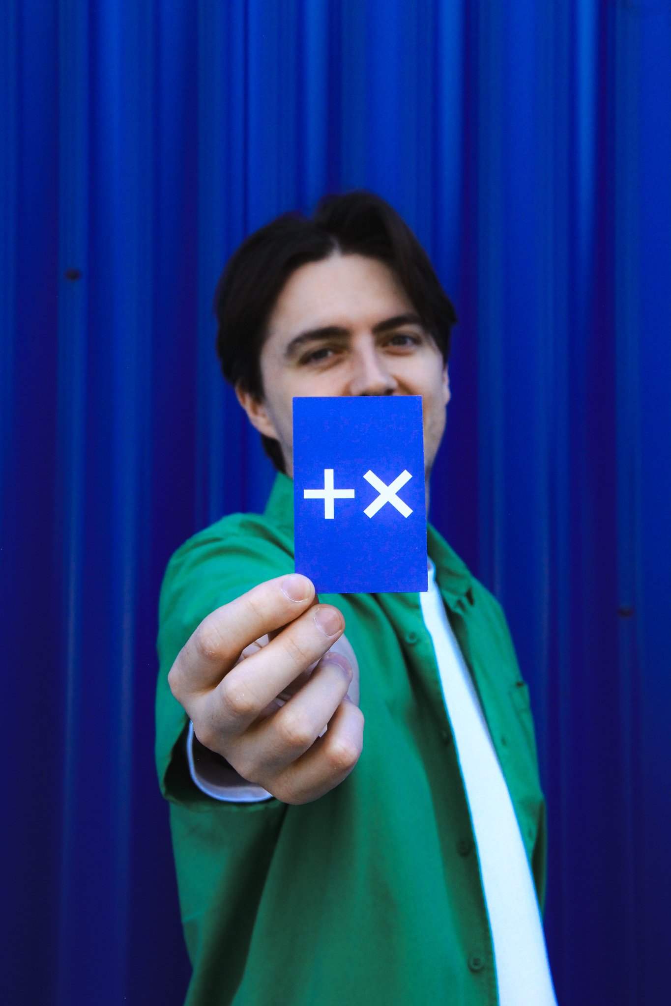 Un homme tenant une carte bleue avec un symbole plus et un symbole de multiplication en blanc, devant un rideau bleu