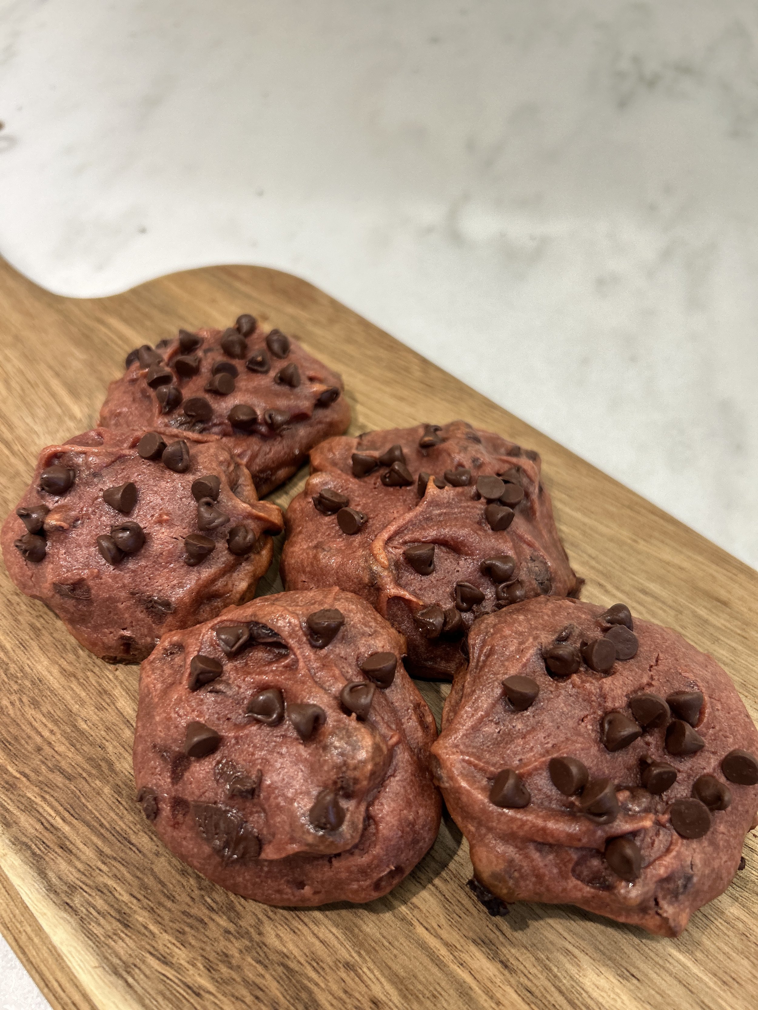 Six chocolate chip cookies on a wooden cutting board.