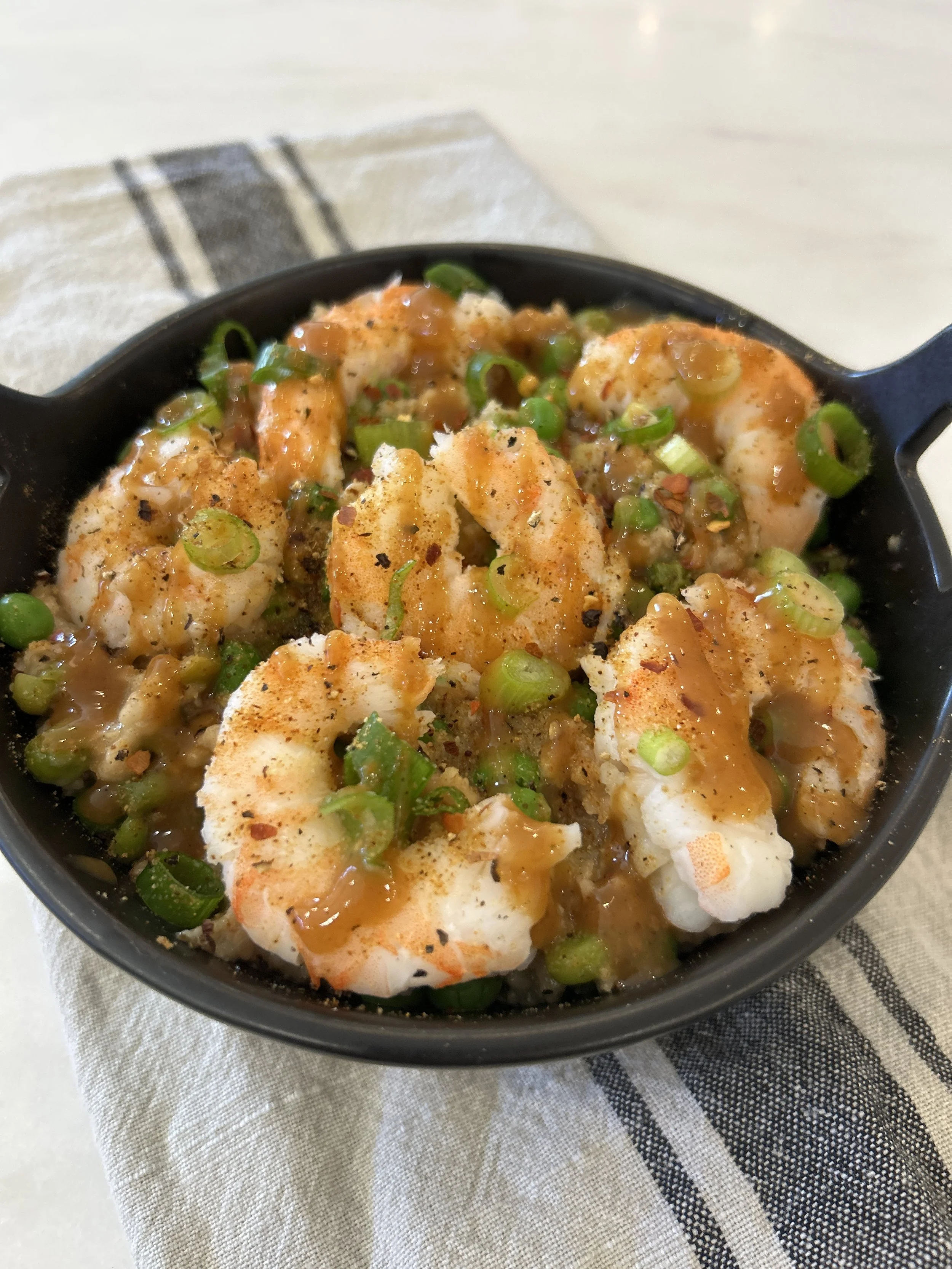 Cooked shrimp garnished with green onions and spices in a black skillet.