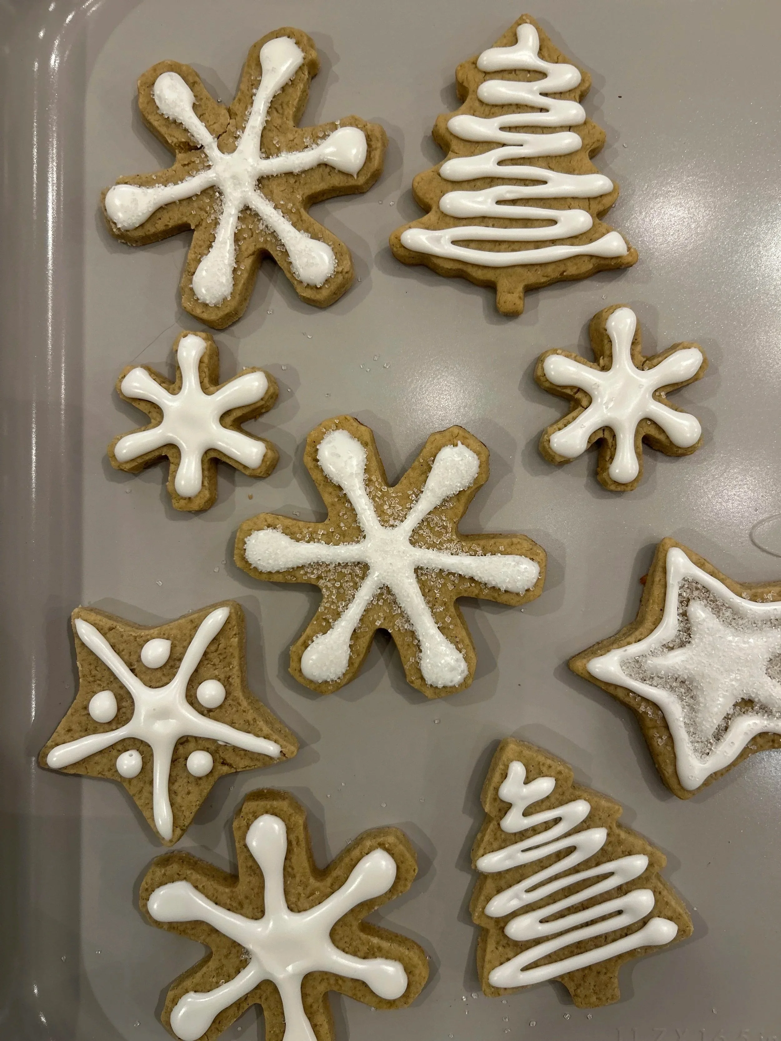Holiday sugar cookies decorated with white icing, shaped like snowflakes, stars, and Christmas trees.