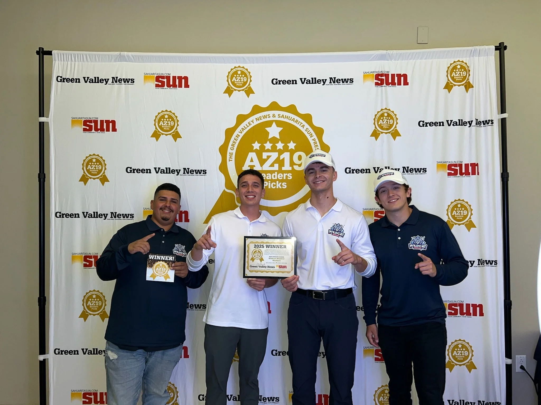 Four young men holding an award and a certificate, standing in front of a backdrop with newspaper logos and awards, celebrating their achievement at an event.