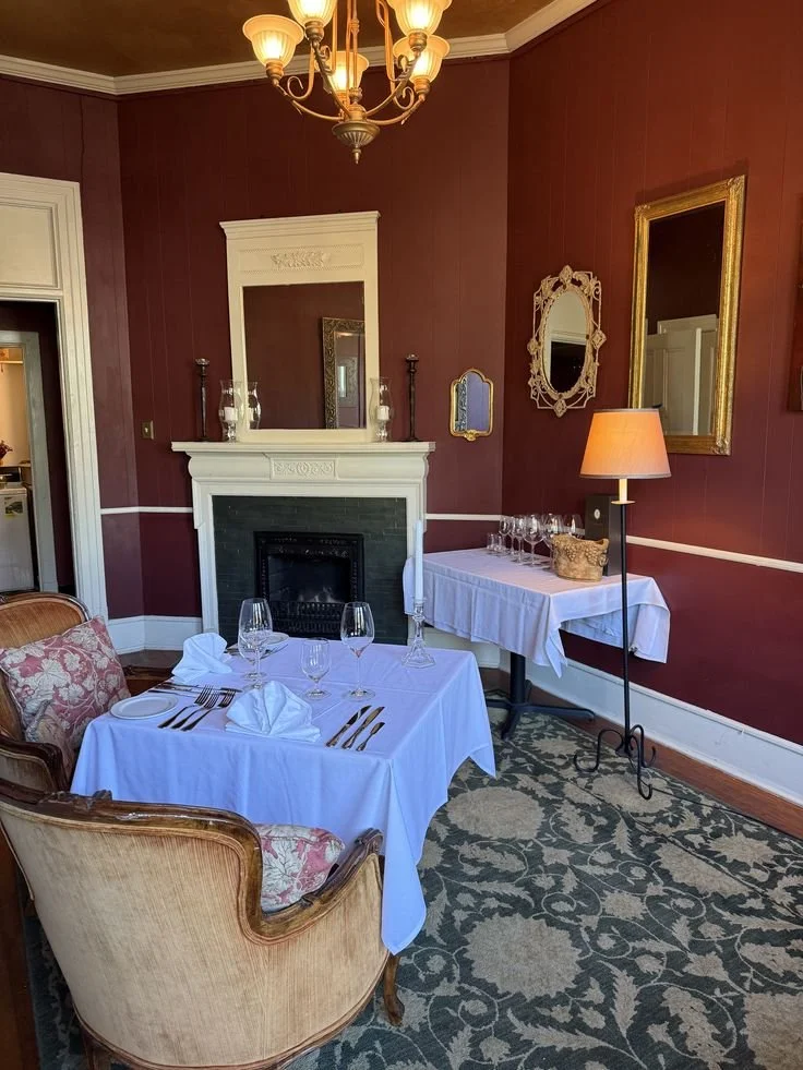 Elegant dining room with a white table set for a meal, surrounded by vintage chairs, with a fireplace, mirrors, and warm lighting.