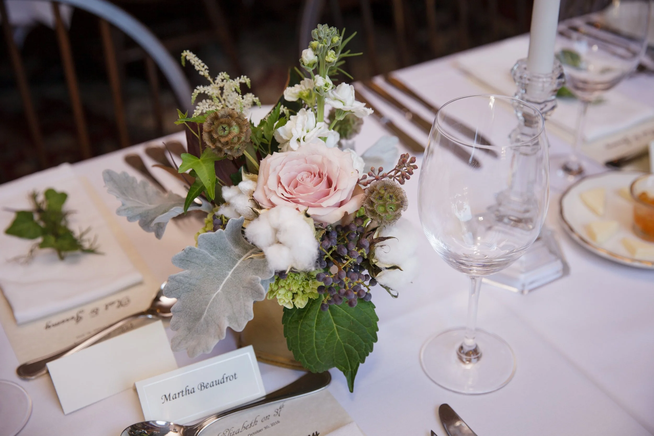 Elegant table setting with a pink rose flower arrangement, wine glass, and cutlery, set for a formal occasion.