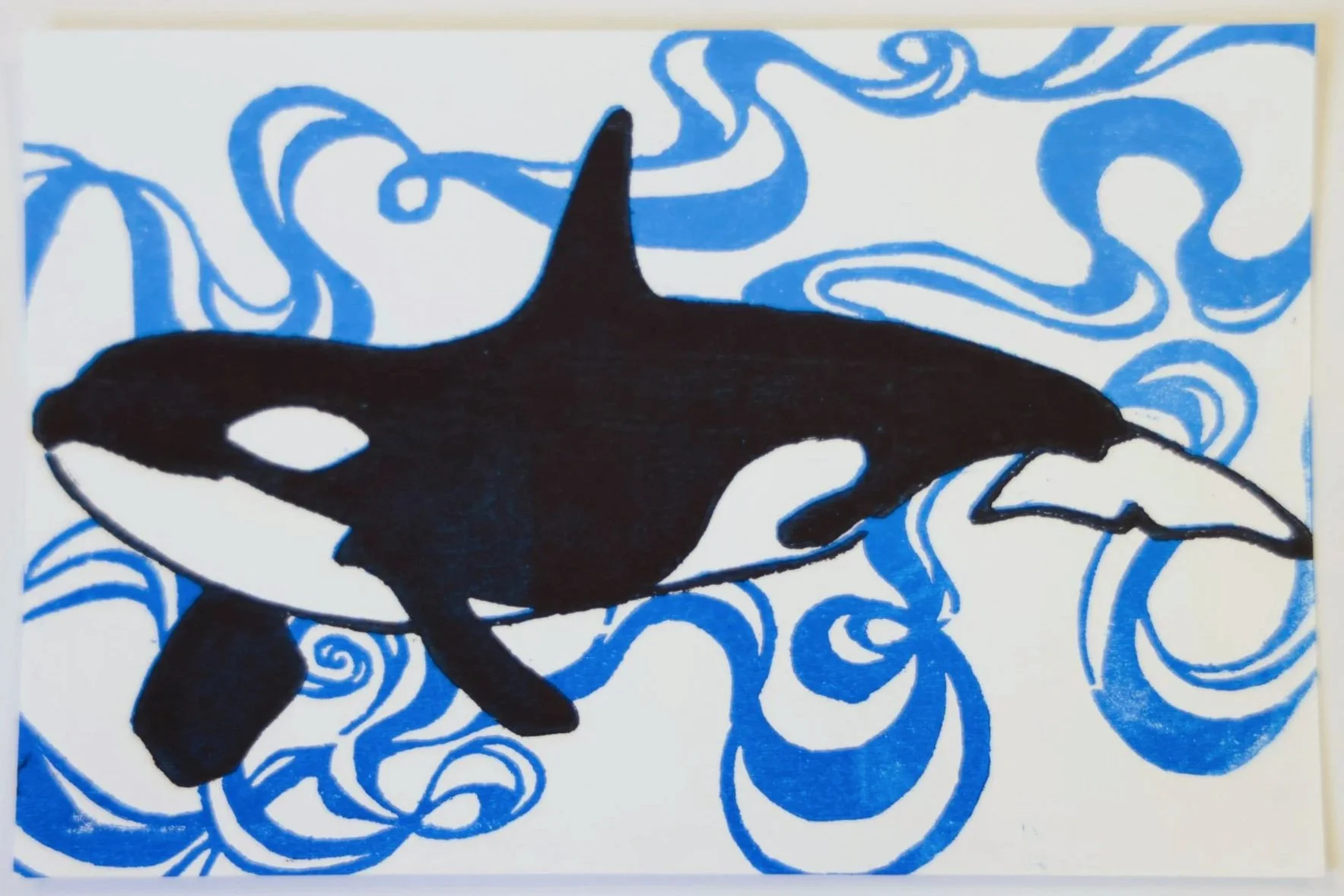 Print of an orca with a slight smile, swimming left. Blue ribbon-like swirls behind the animal remind of water.