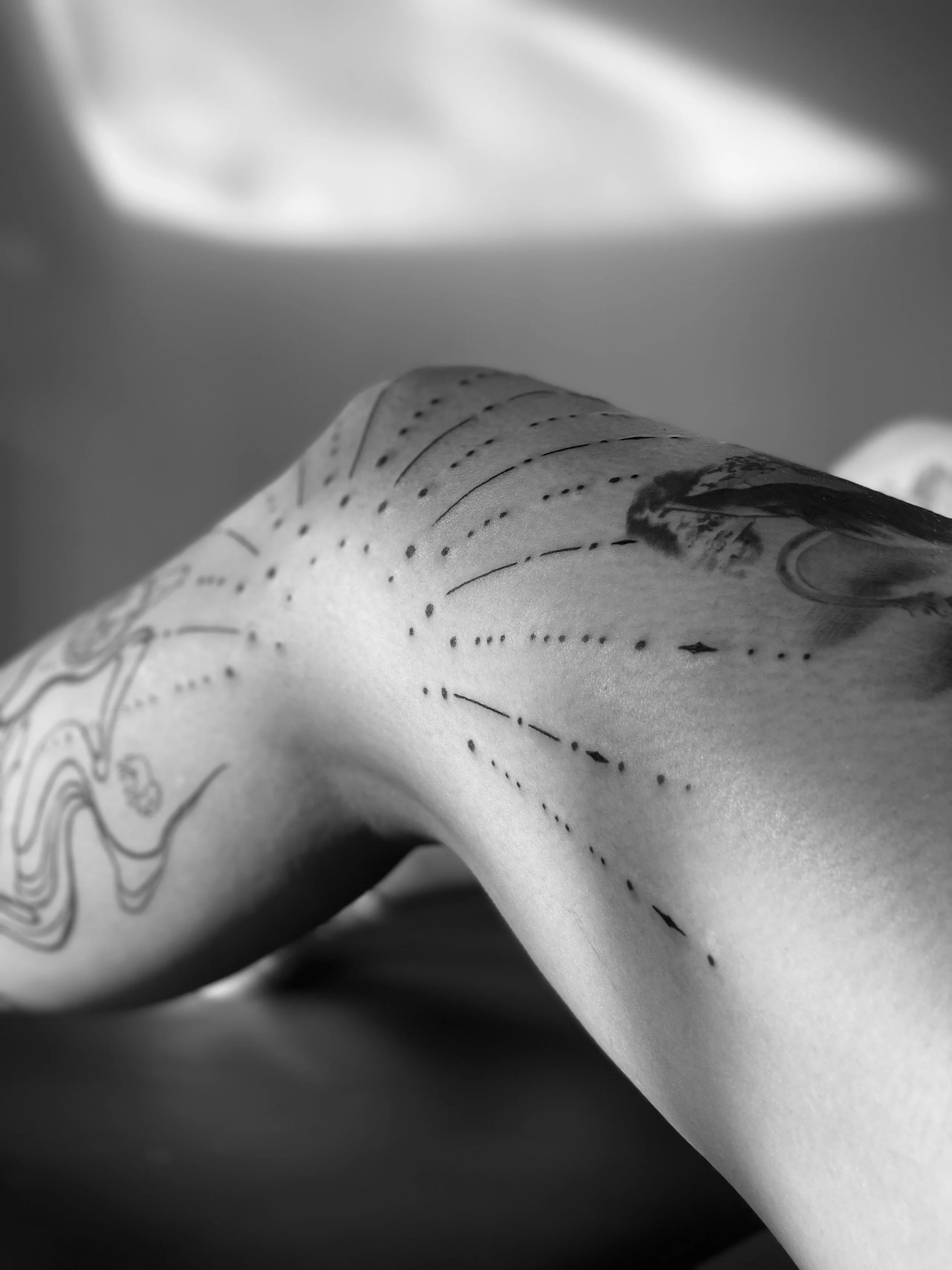 Close-up black and white photo of a tattooed arm, with dotted lines indicating a guide for tattooing.