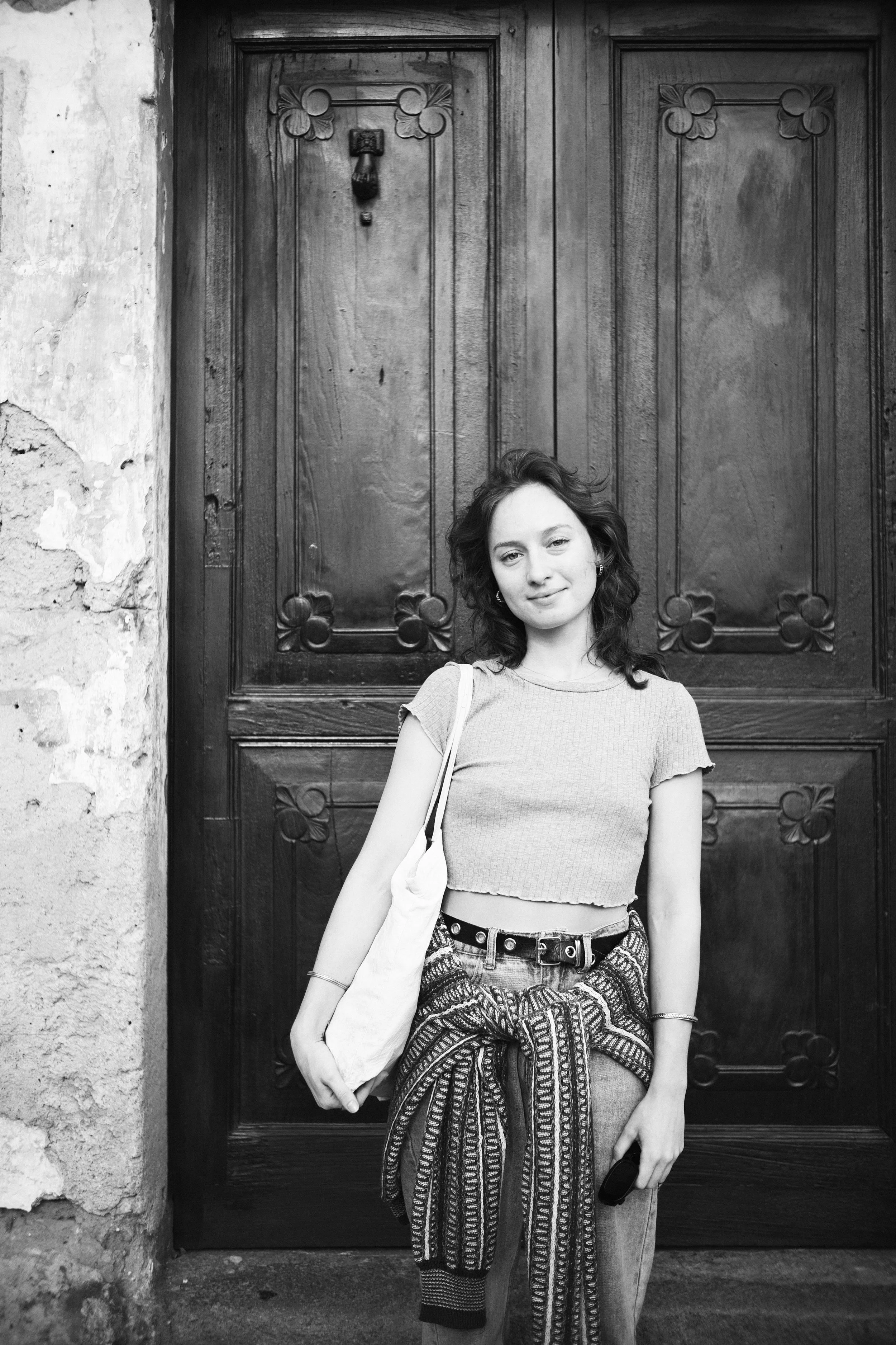 A woman with curly hair standing in front of a wooden door with decorative carvings.