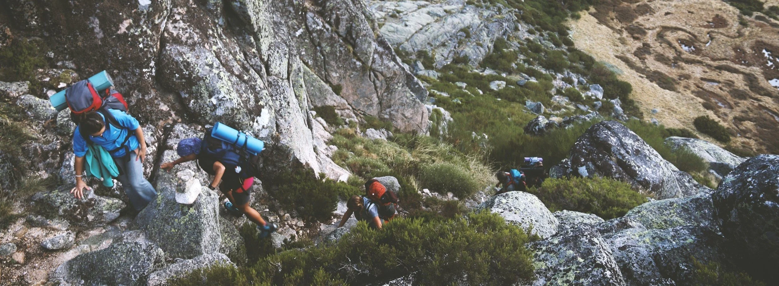 A group of hikers climbing a rocky and steep mountain trail with backpacks and outdoor gear.