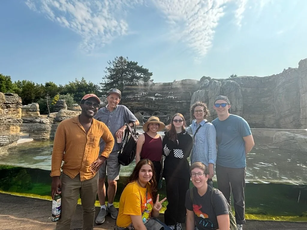 Union Youth Group event with eight people posing outdoors near water and rock formations on a bright sunny day.