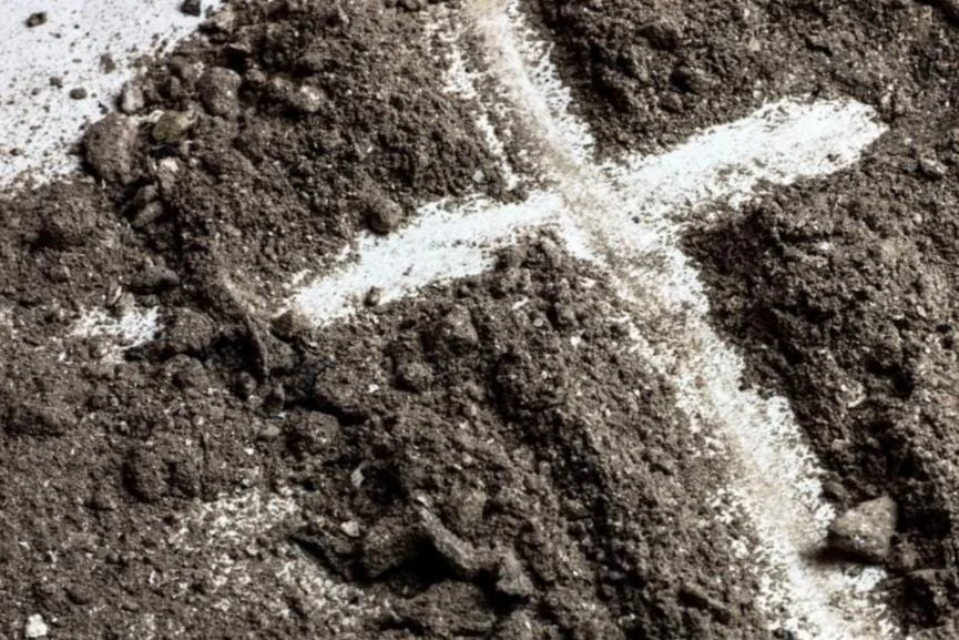 A white cross in the midst of ash/dirt, symbolizing Ash Wednesday service.