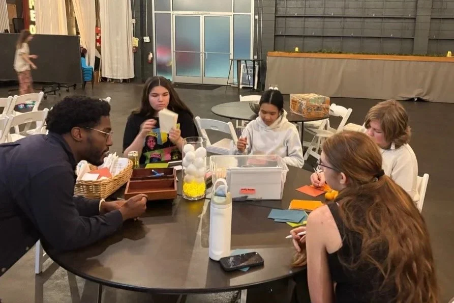 At Union youth group, a man (Pastor Phil) leans on a table and is speaking with four youth who all are working on craft paper.