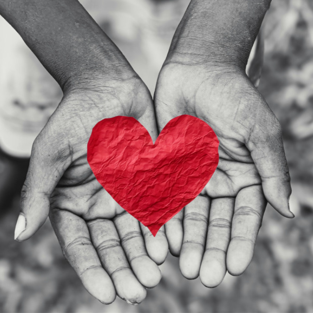 Two hands are cupped together, and a red wrinkled heart is being held in the hands