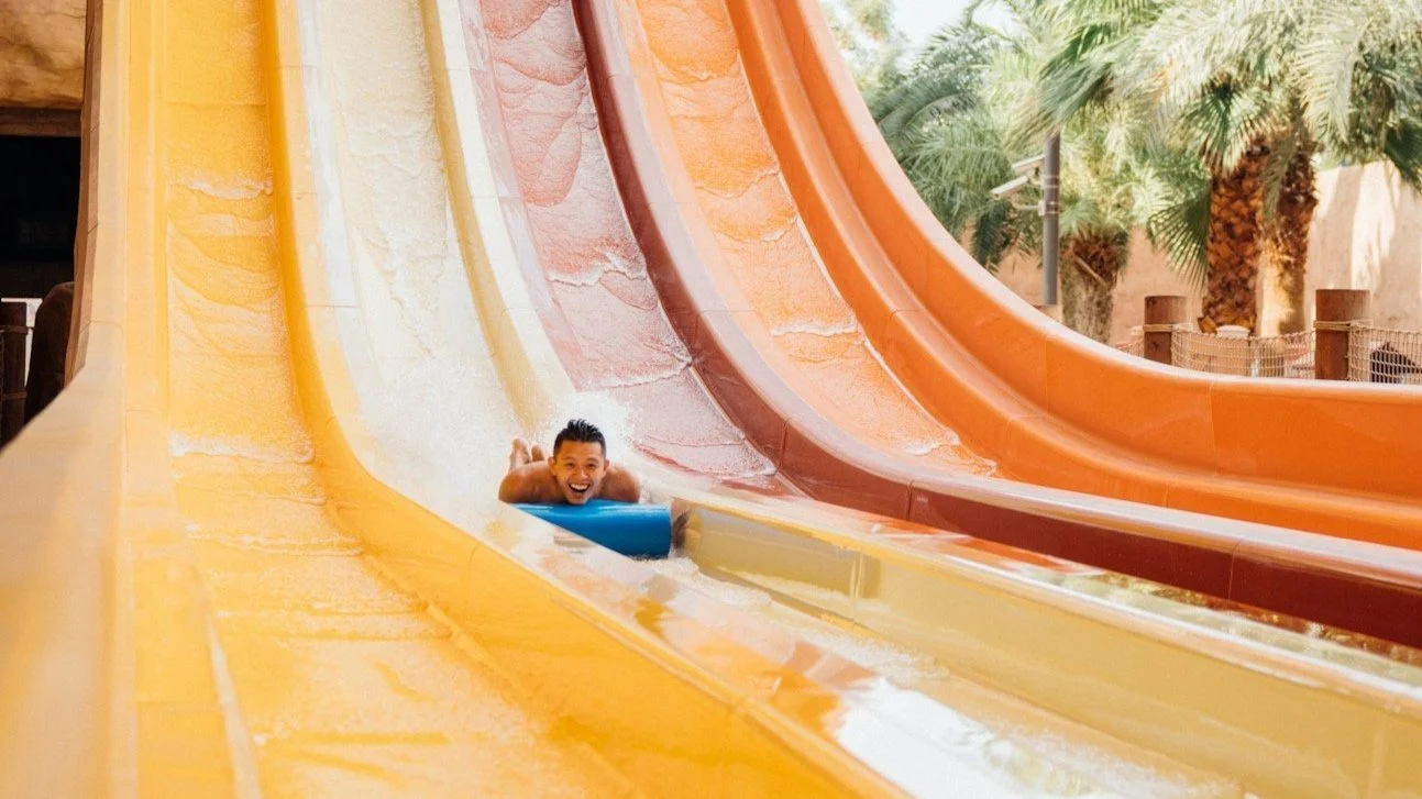 Man smiling while riding a water slide at Wild Waves Theme Park — join The Table youth group summer outing