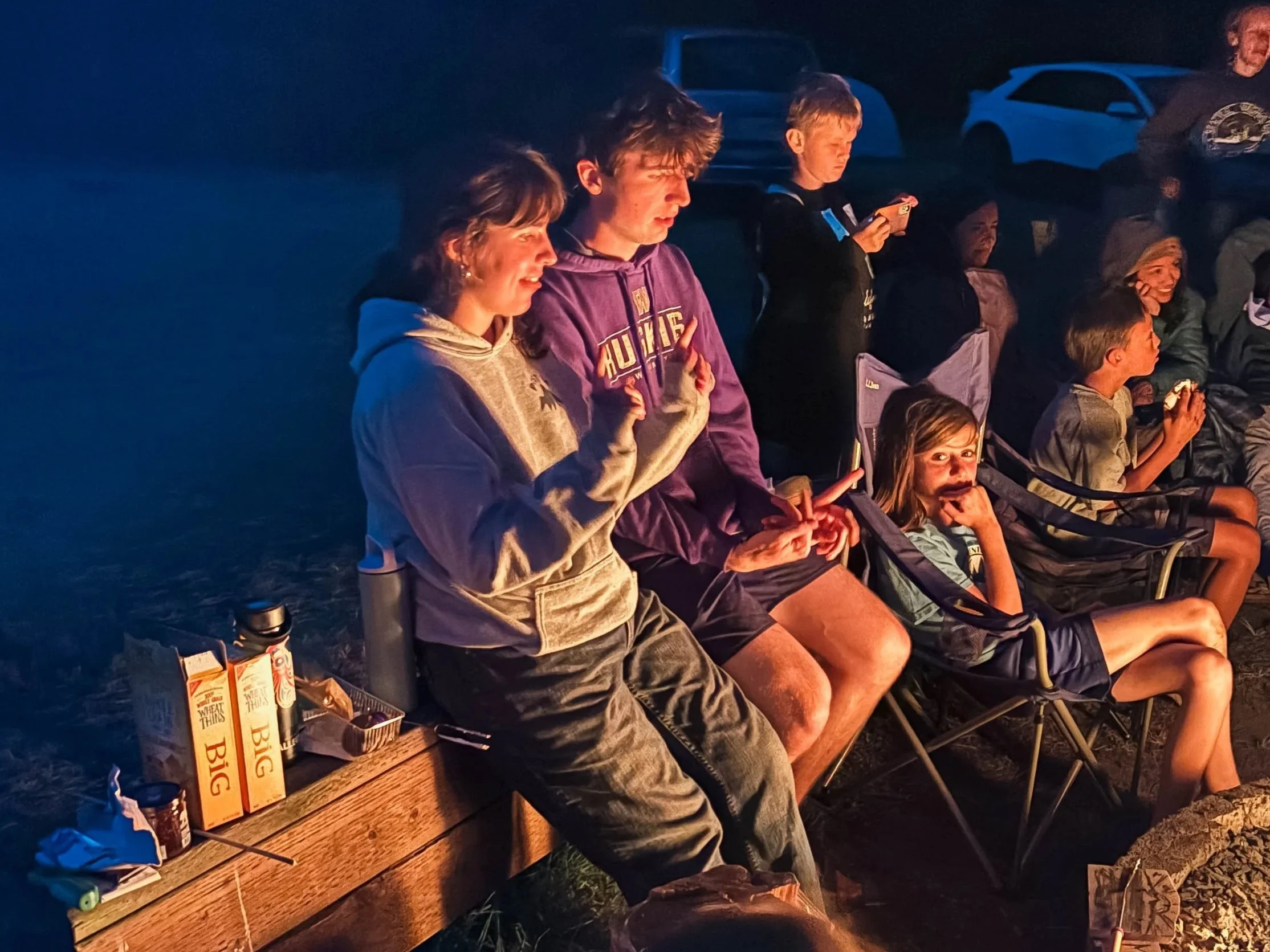 A group gather at night around a campfire, for smores and laughter.