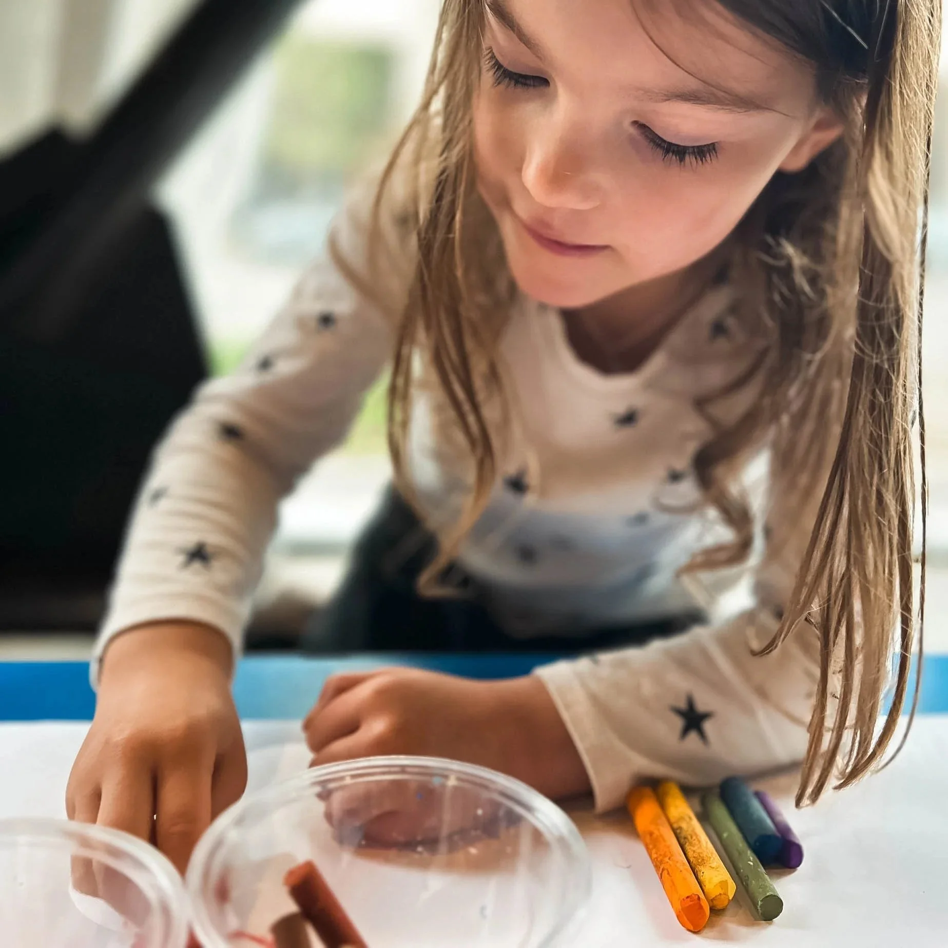 A close up of a young girl looking down at a paper as she colors with brightly colored crayons.