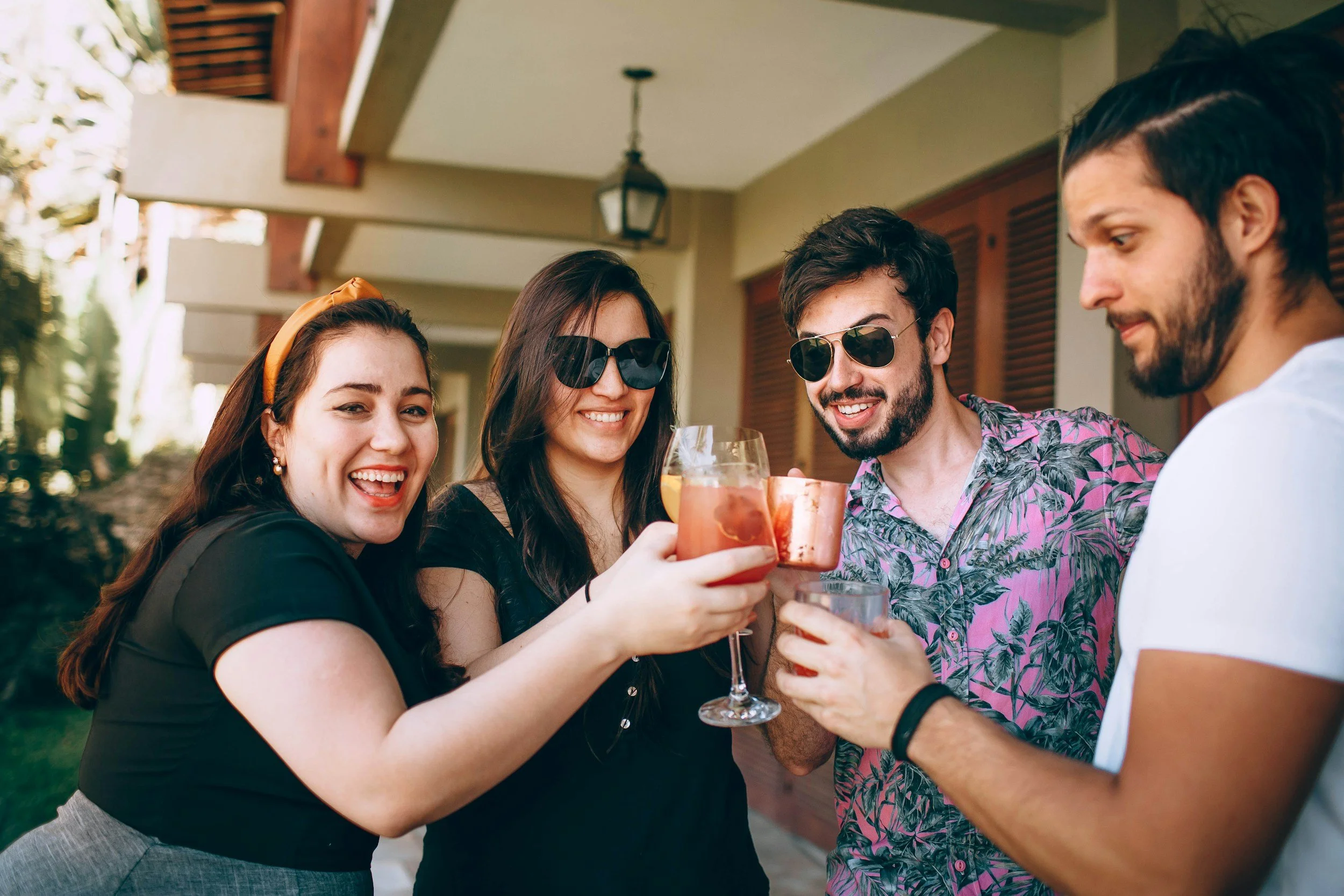 Group of four friends celebrating with drinks on porch, smiling and toasting.