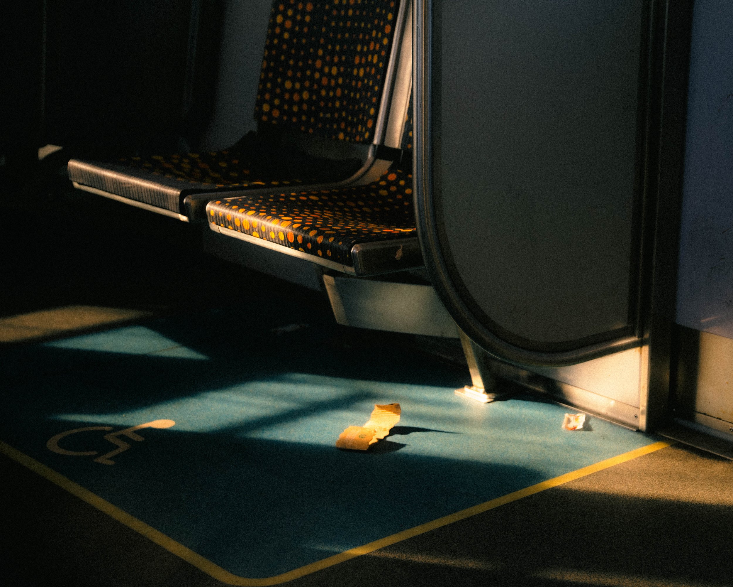 Empty subway train with a wheelchair accessible spot marked on the floor, lit by a dim light with a piece of trash on the floor.