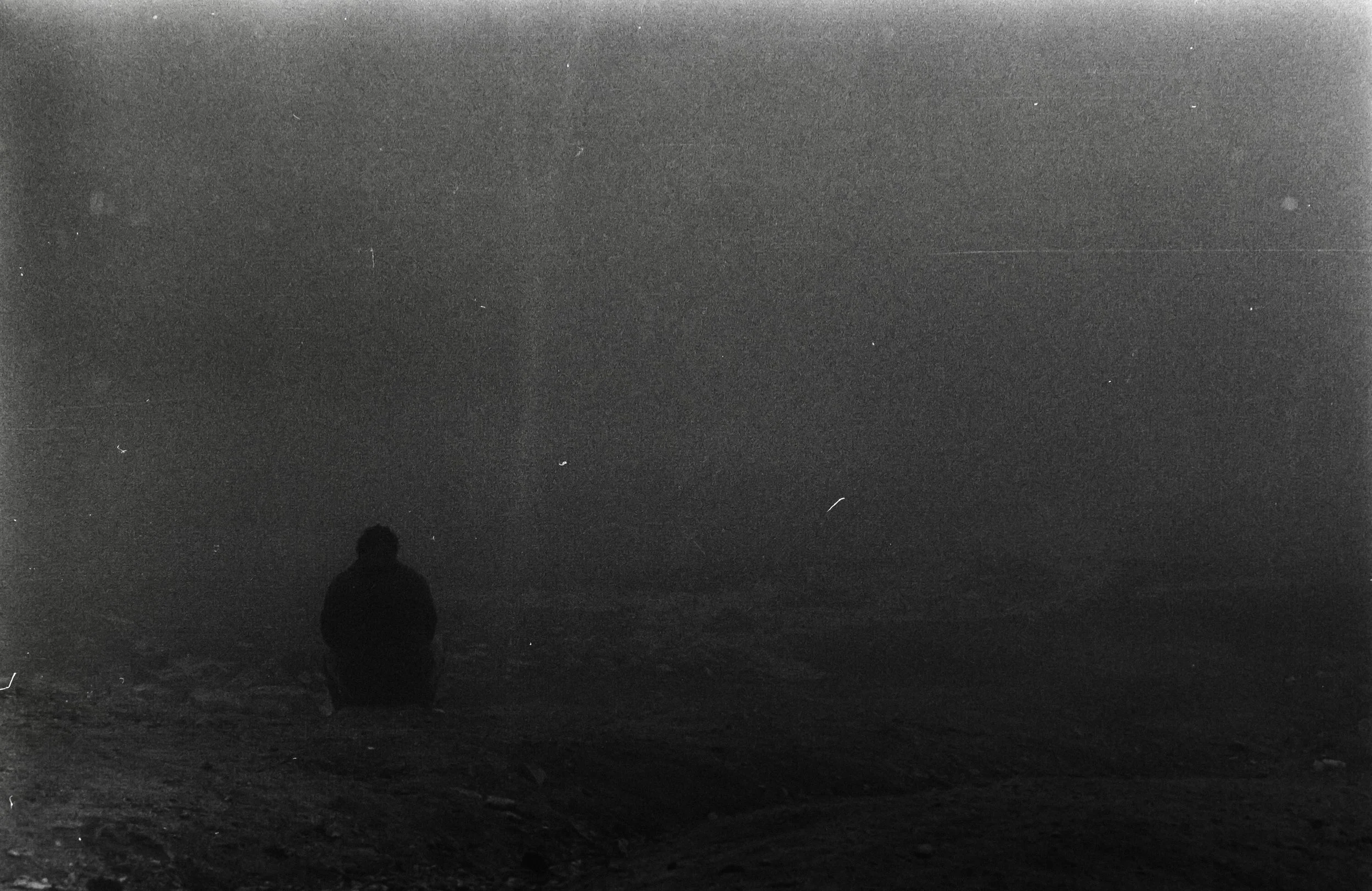 A silhouette of a person kneeling on a beach at night, looking into the distance.