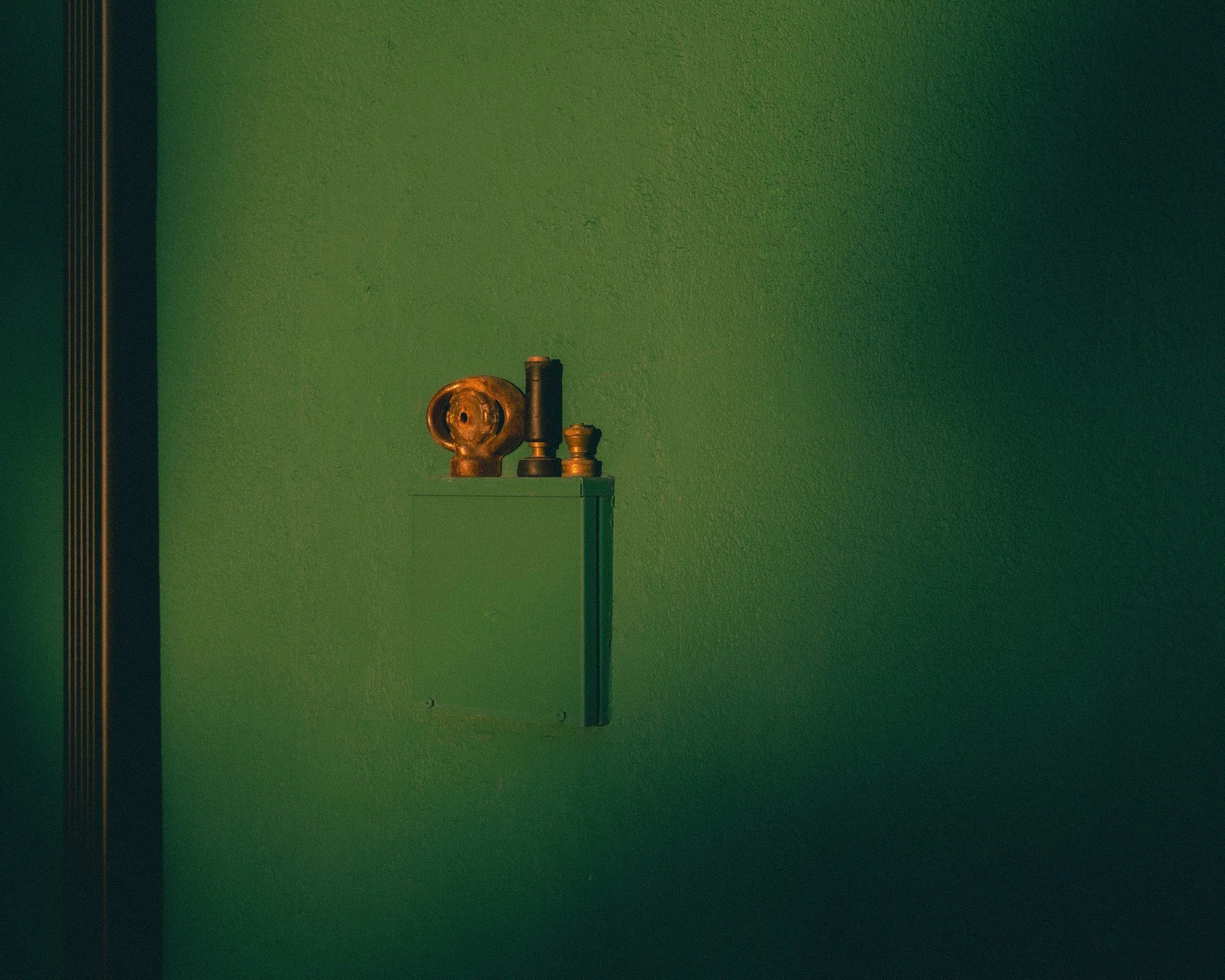 A green wall with a cardboard box containing various antique brass objects on top, near the left side of the image.