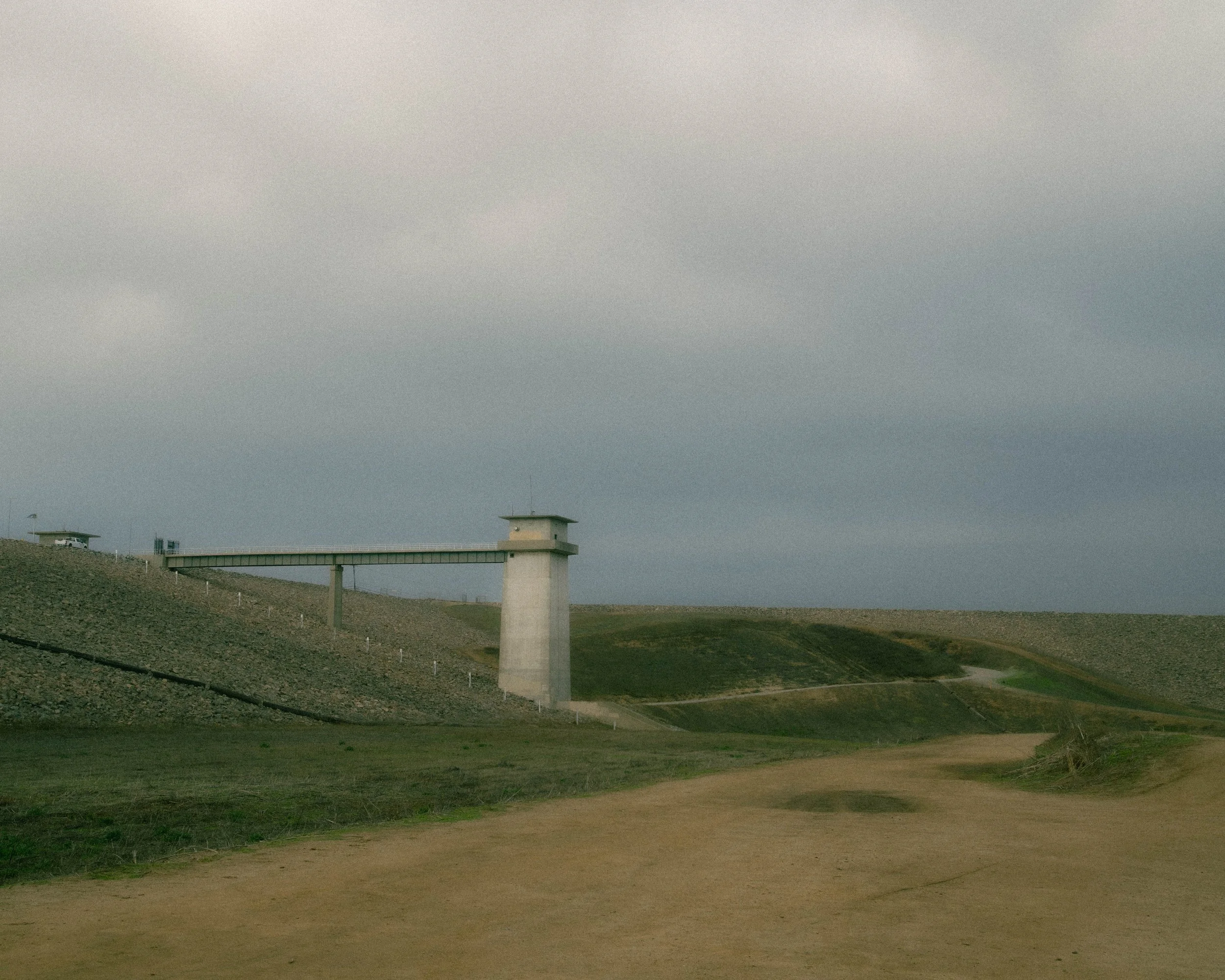 View of a security watchtower on a sloped hill with a dirt path in foreground and a cloudy sky overhead.