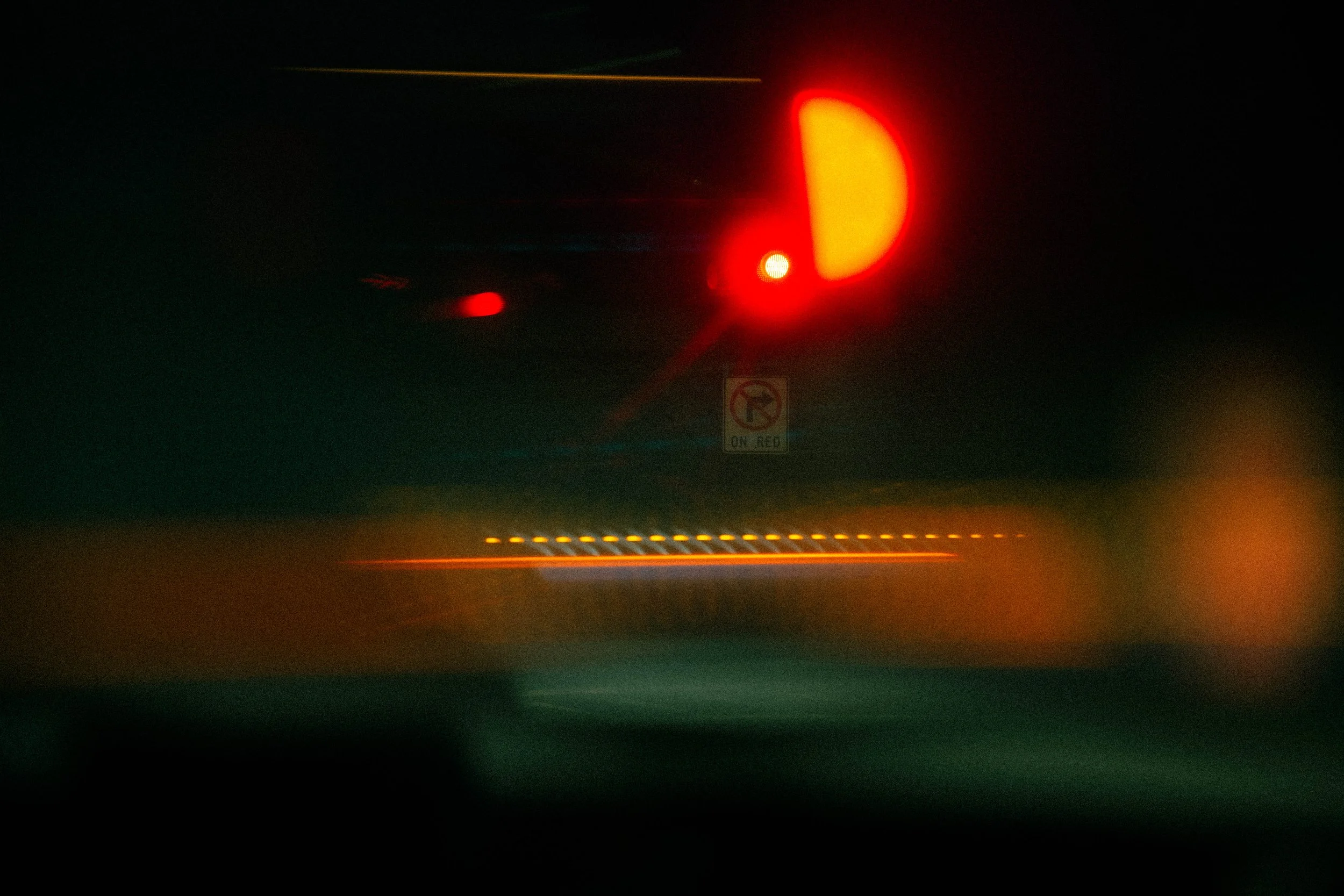 Blurred view of a vehicle's tail lights at night, with a no U-turn sign and streaks of red, yellow, and green lights.