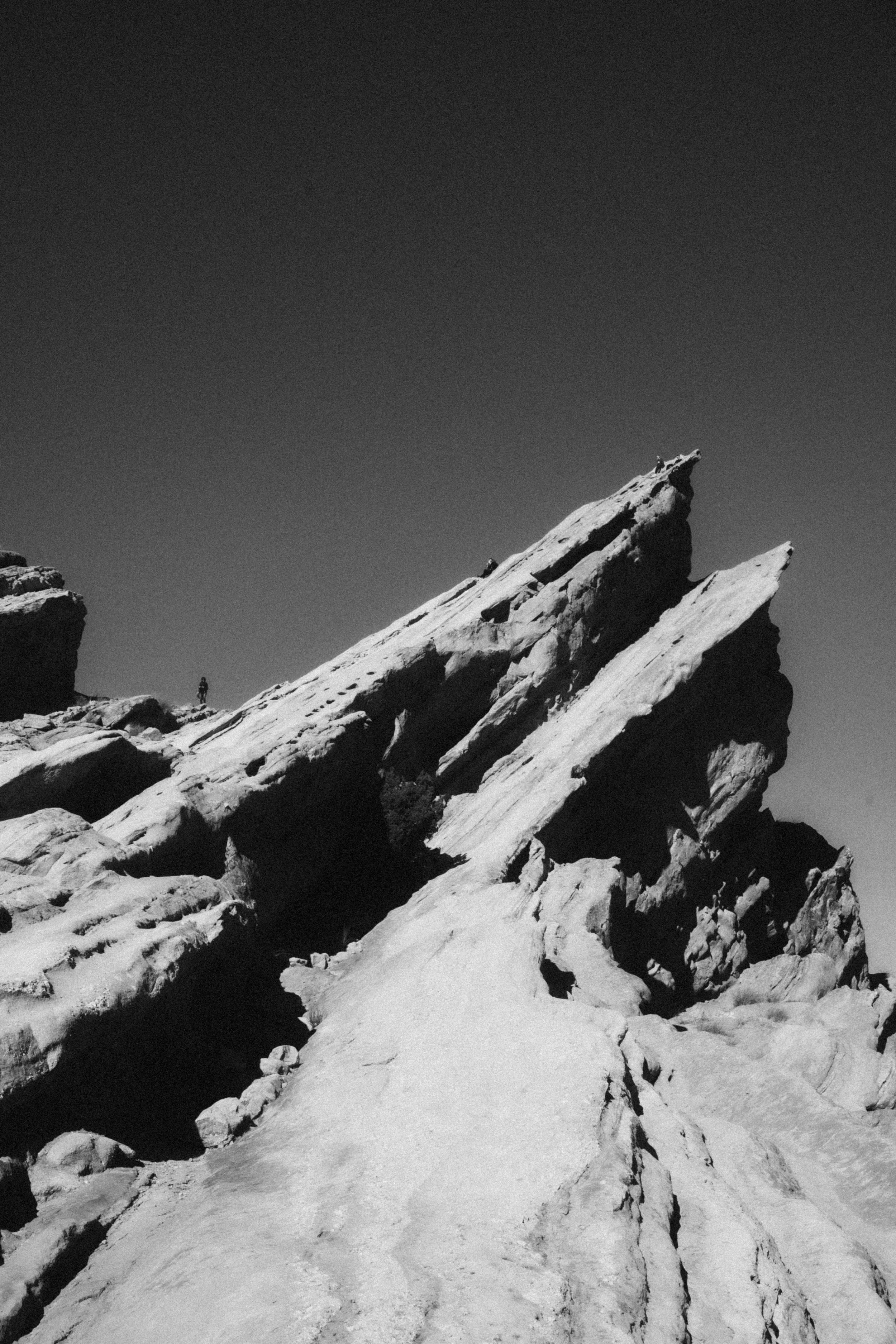 Black and white photo of a rocky mountain landscape with jagged rock formations and a lone hiker in the distance.
