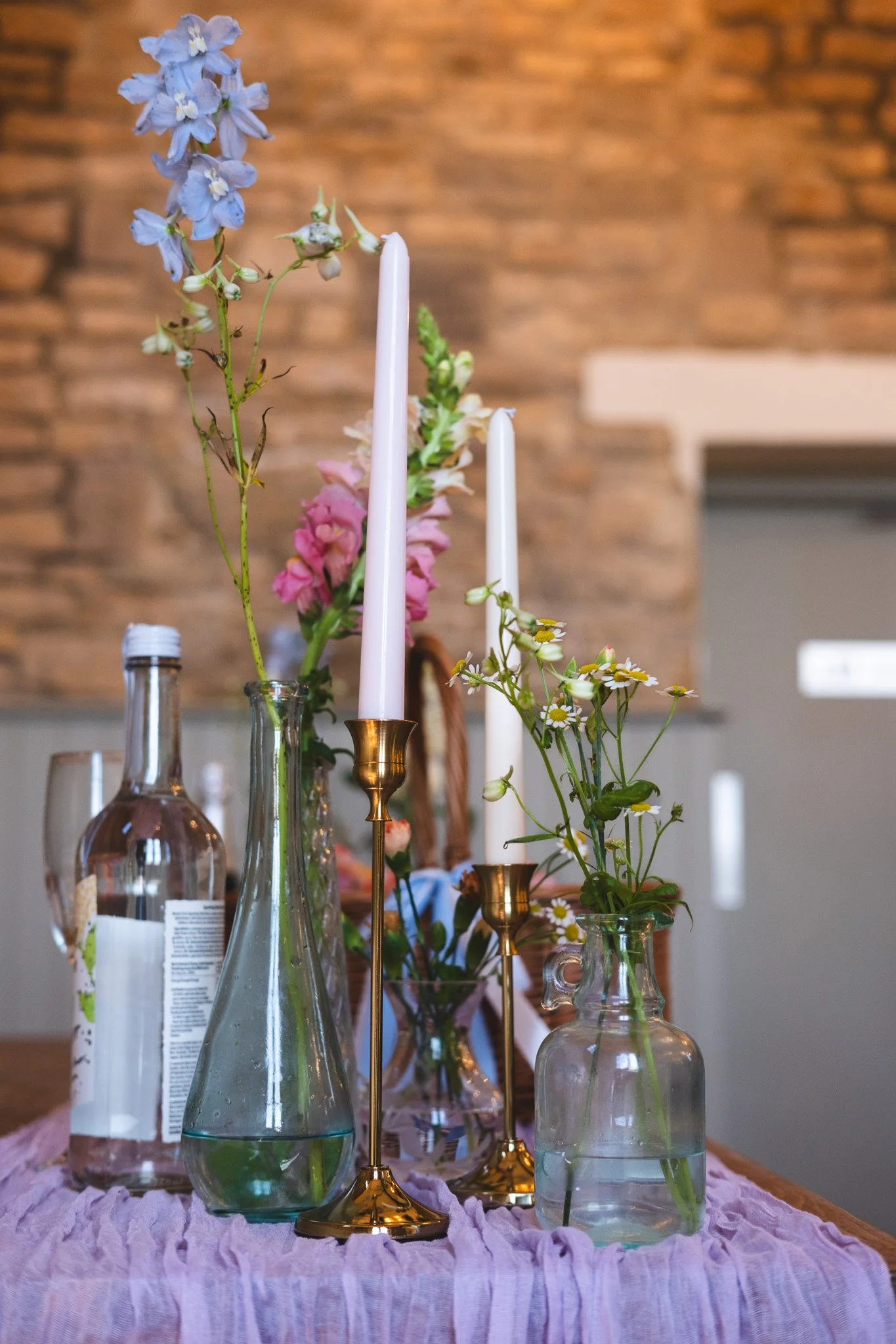 Vases with colorful flowers and tall candles on a table covered with a pink cloth.