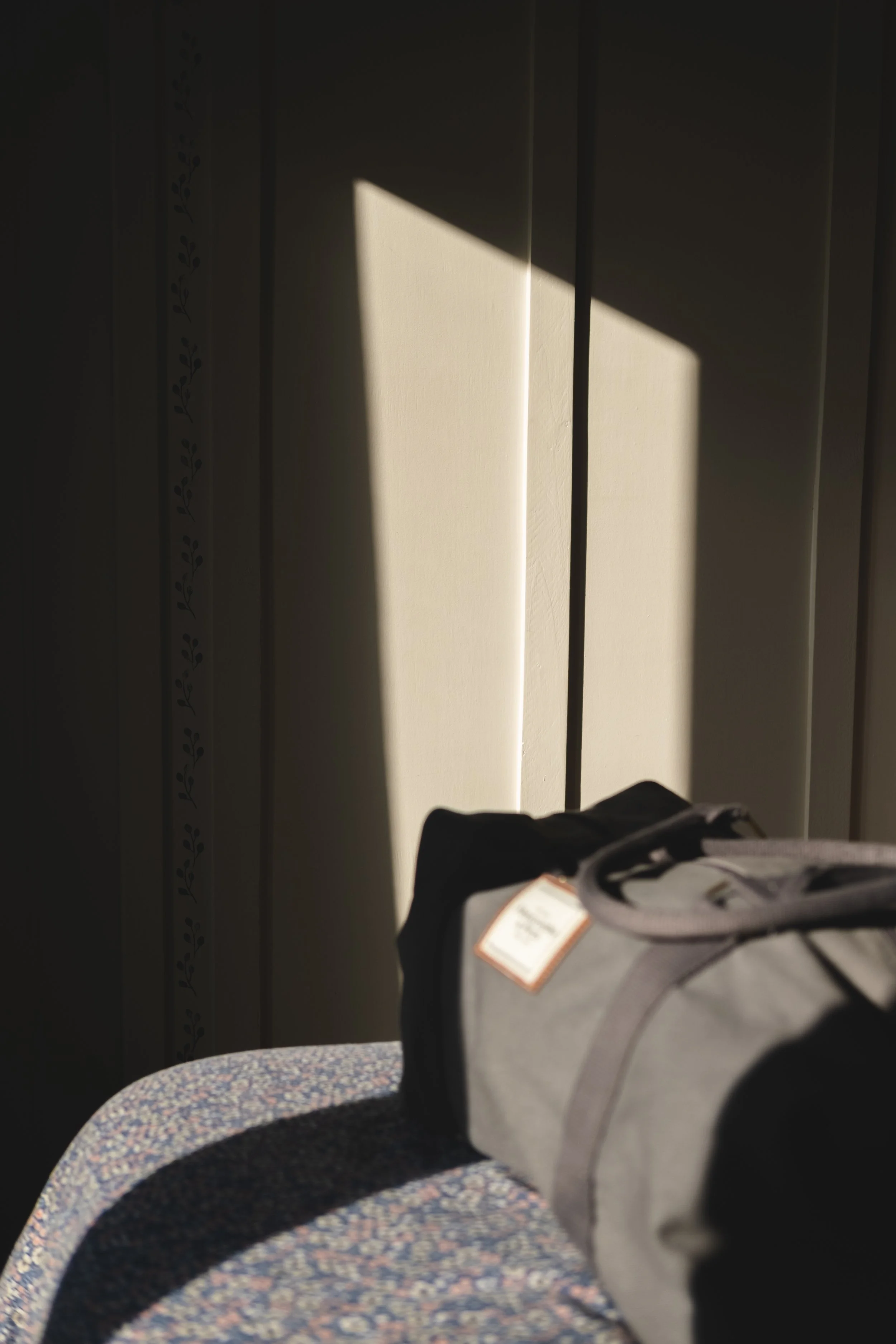 A black and gray duffel bag resting on a blue speckled bench, with sunlight casting shadows from blinds onto a white wall.