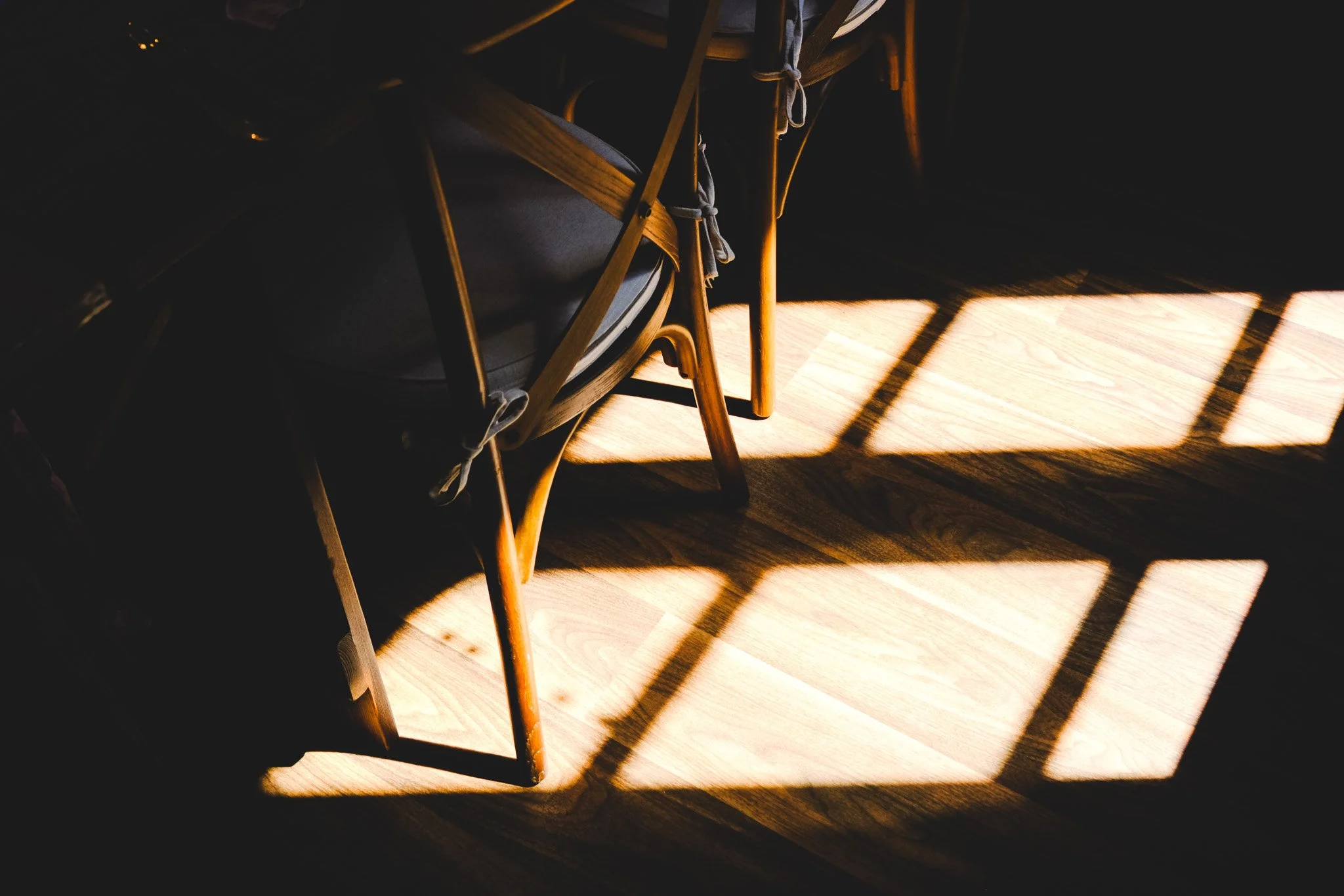 Sunlight casting a grid-shaped shadow of a wooden chair and table on a wooden floor.