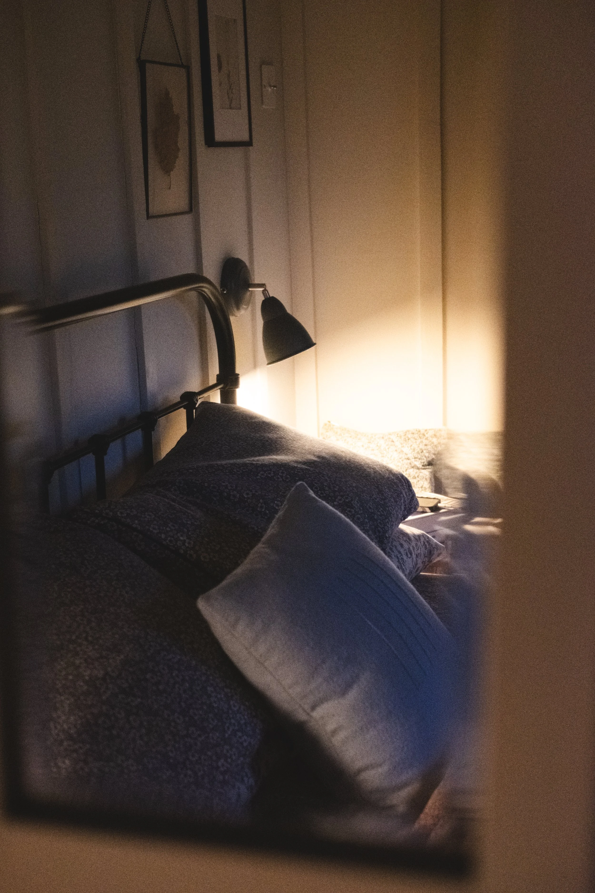 A bed with patterned and solid pillows, illuminated by a bedside lamp, with wall art above the bed.