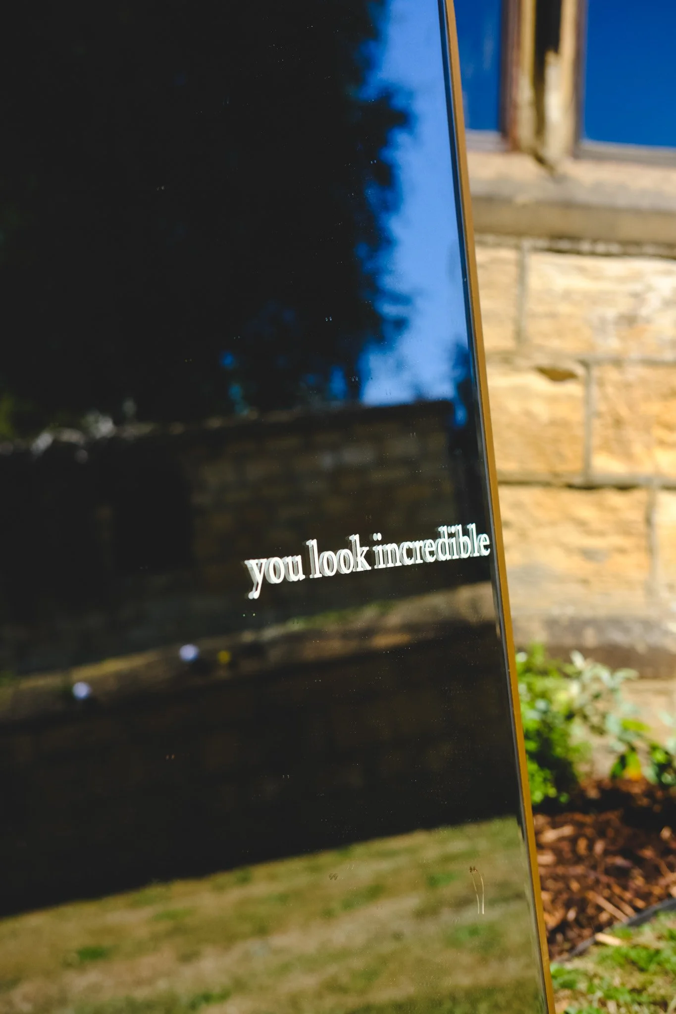 Close-up of a smartphone screen displaying the message 'you look incredible' against a background of trees and sky visible in the reflection.