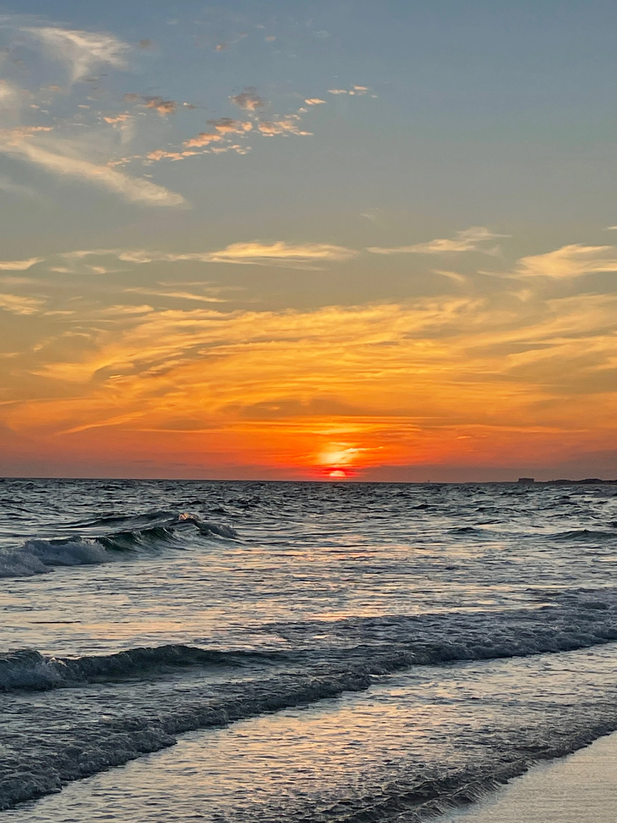 Sunset over the ocean with colorful sky and gentle waves.