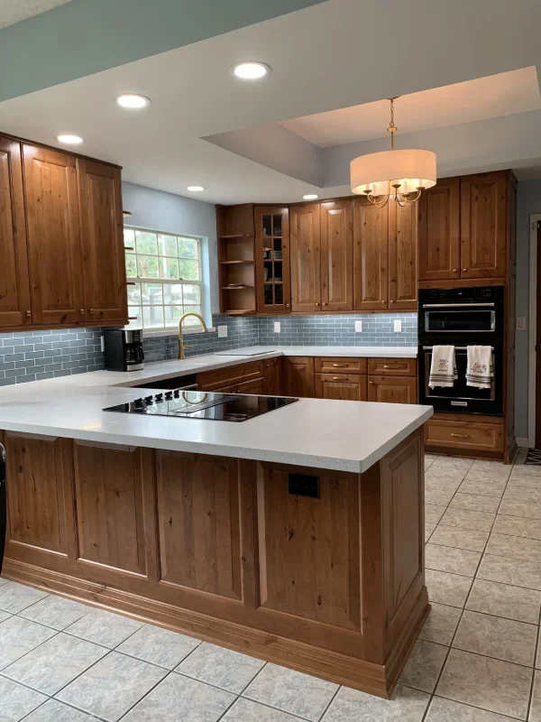 Kitchen with wooden cabinets, a white countertop island, blue subway tile backsplash, stainless steel sink, black stove, a breakfast nook, large window, and tile flooring.
