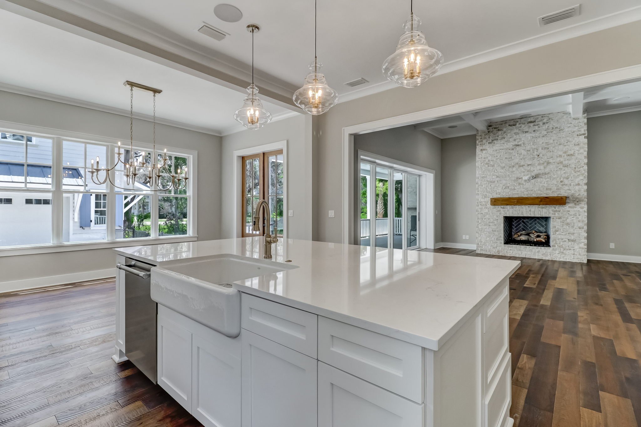 Modern kitchen with white island, large windows, sculptural pendant lights, and a white brick fireplace in the living area.