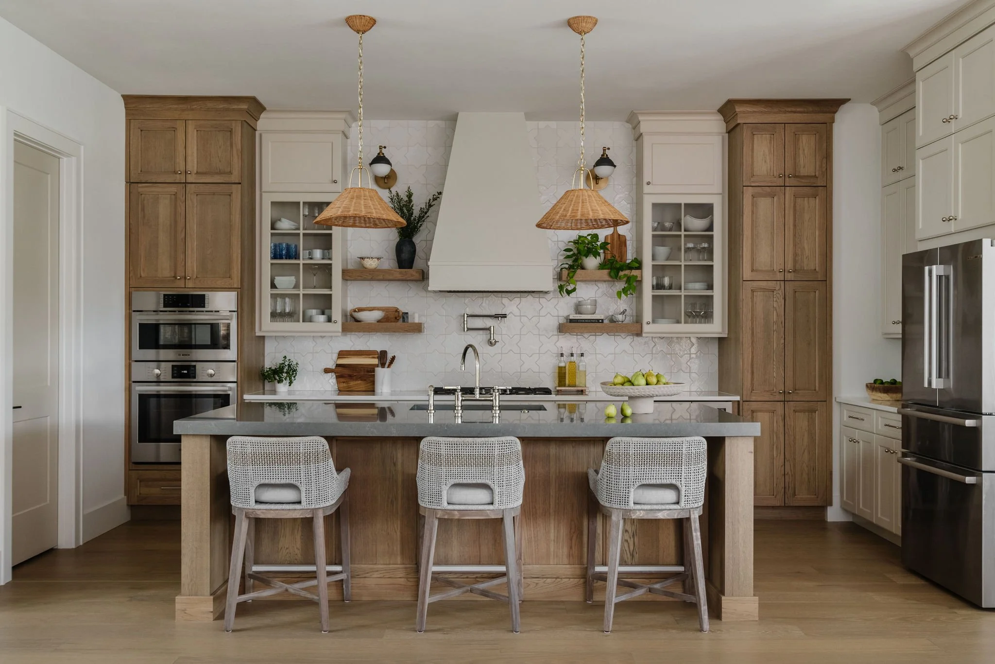 Modern kitchen with wooden and white cabinets, pendant lights, a kitchen island with seating, and decorative shelving with plants and dishes.